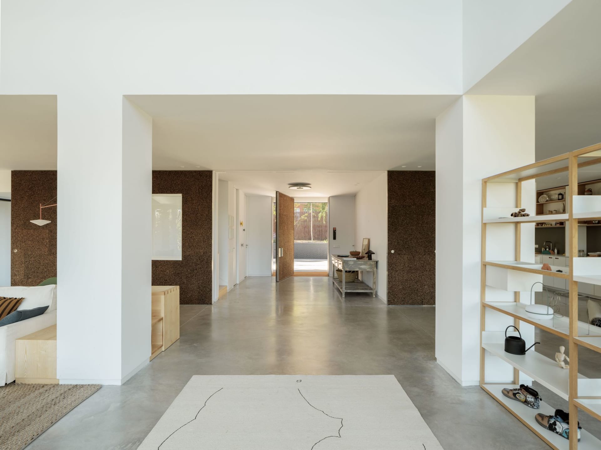 Modern living room with concrete flooring, wooden furniture, and textured cork walls.