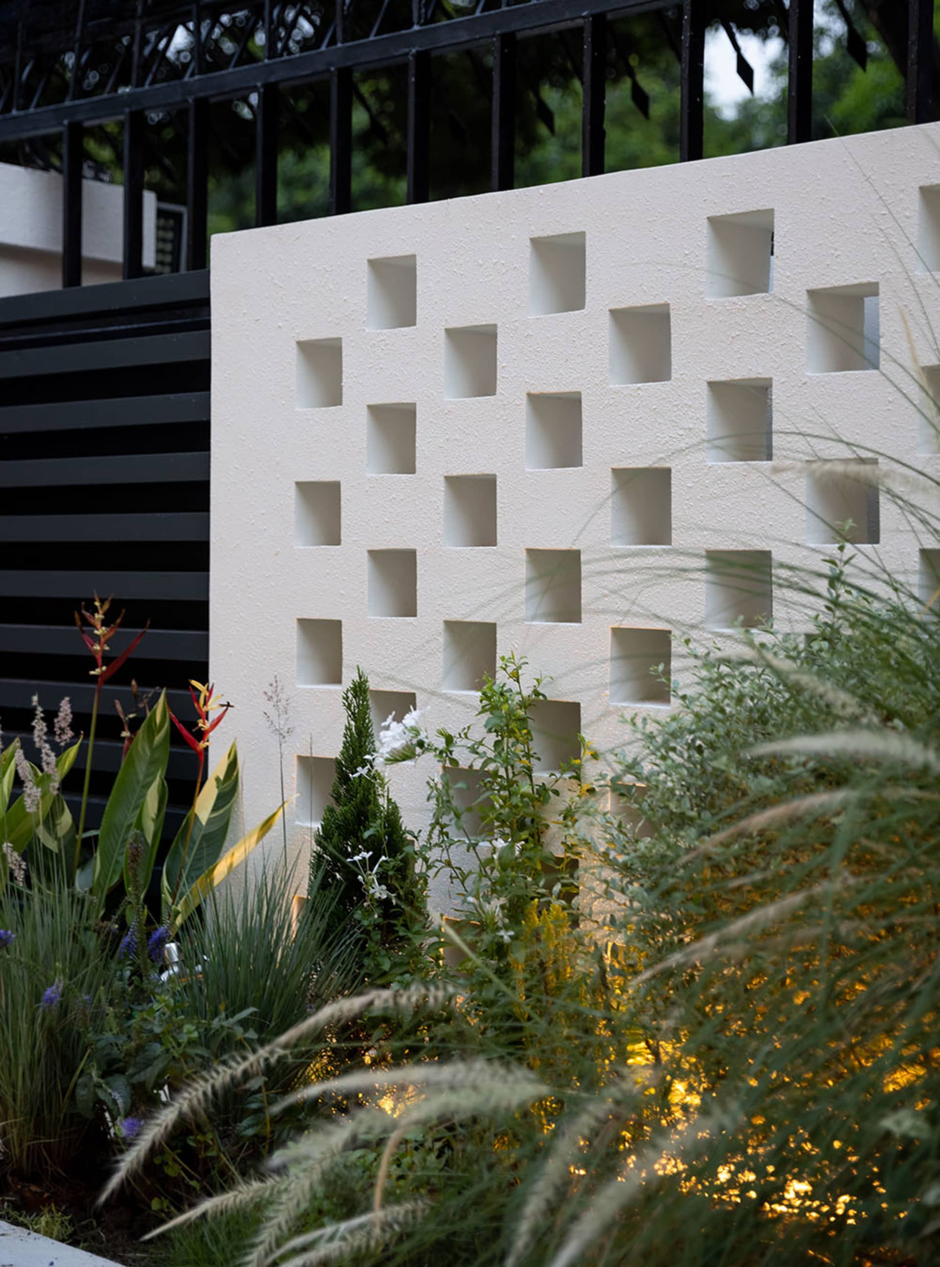 A concrete garden screen with a grid of rectangular cutouts, surrounded by greenery.