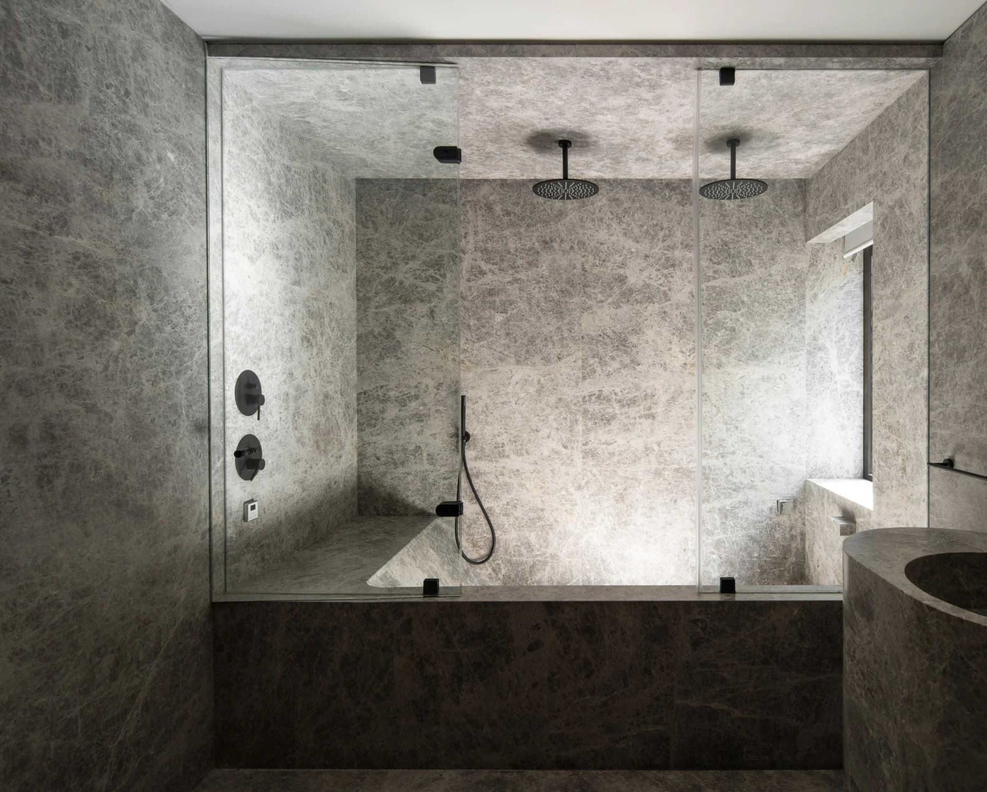 Modern minimalist bathroom with marble finishes, featuring a glass-enclosed shower and sleek black fixtures.