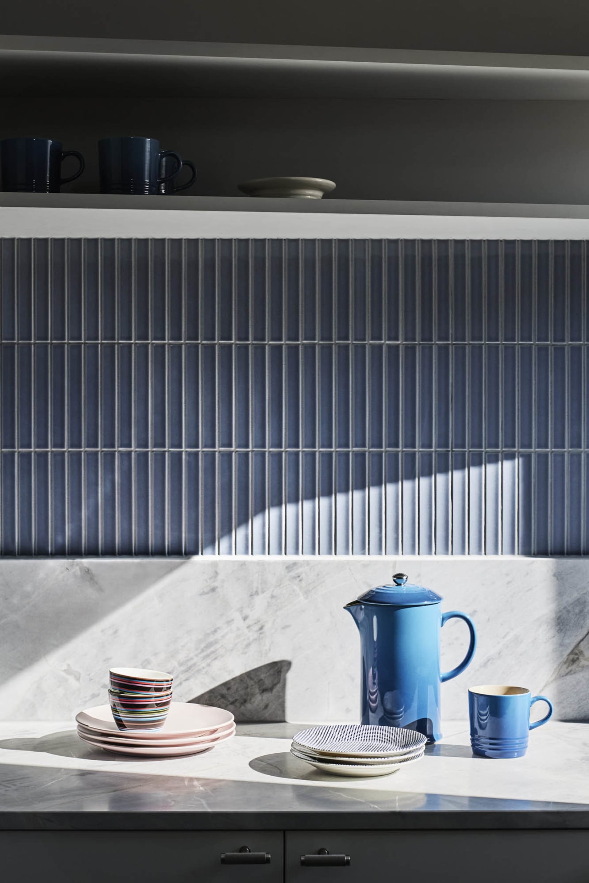 A modern kitchen featuring ceramic plates, bowls, and mugs on a marble countertop with blue accents.