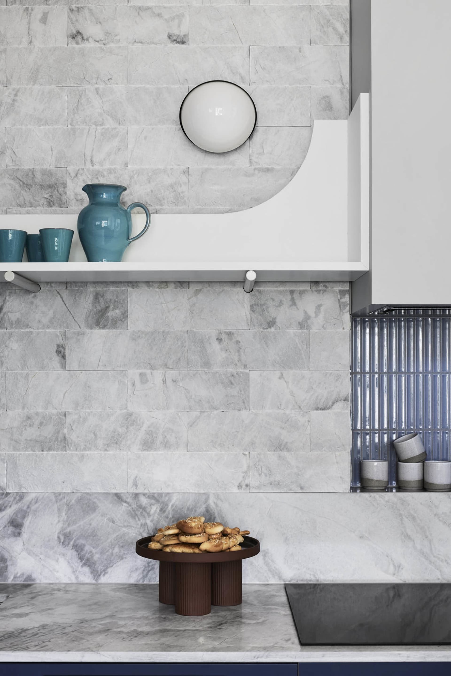 Marble kitchen counter with blue utensils and a brown bowl of pastries.