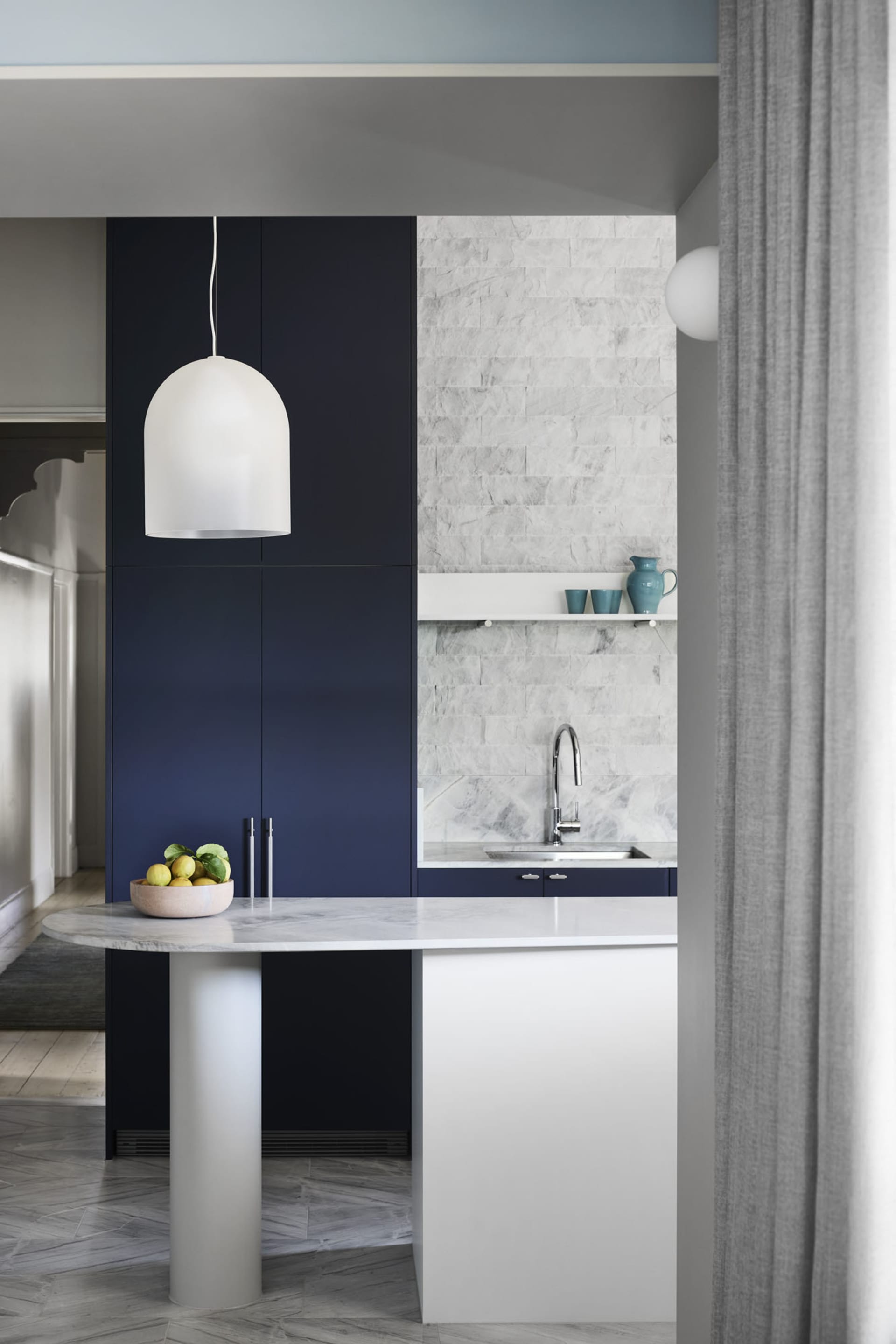 A modern kitchen with a marble countertop and navy blue cabinets.