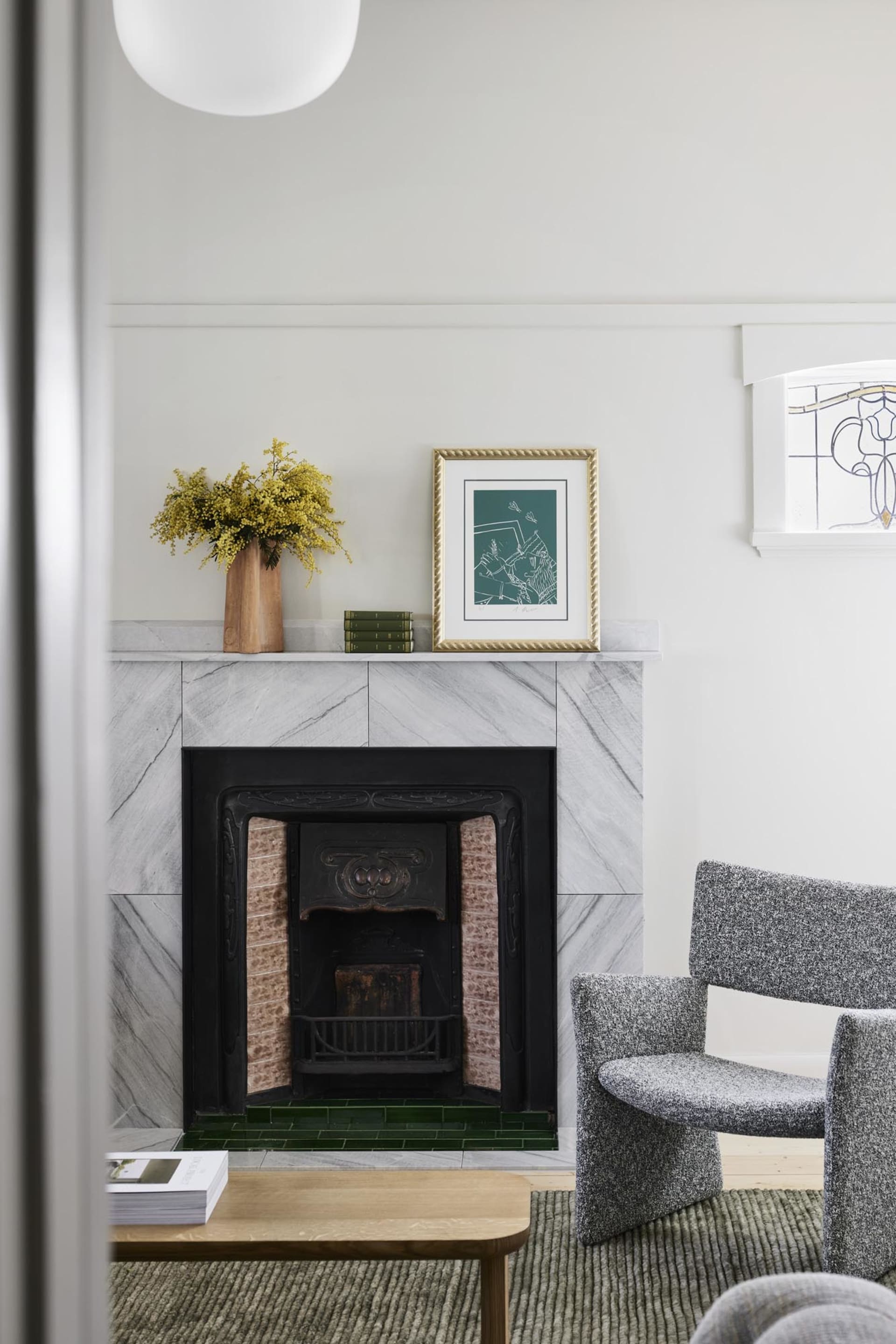 A modern living room with marble fireplace, grey armchairs, and green vase on mantel.