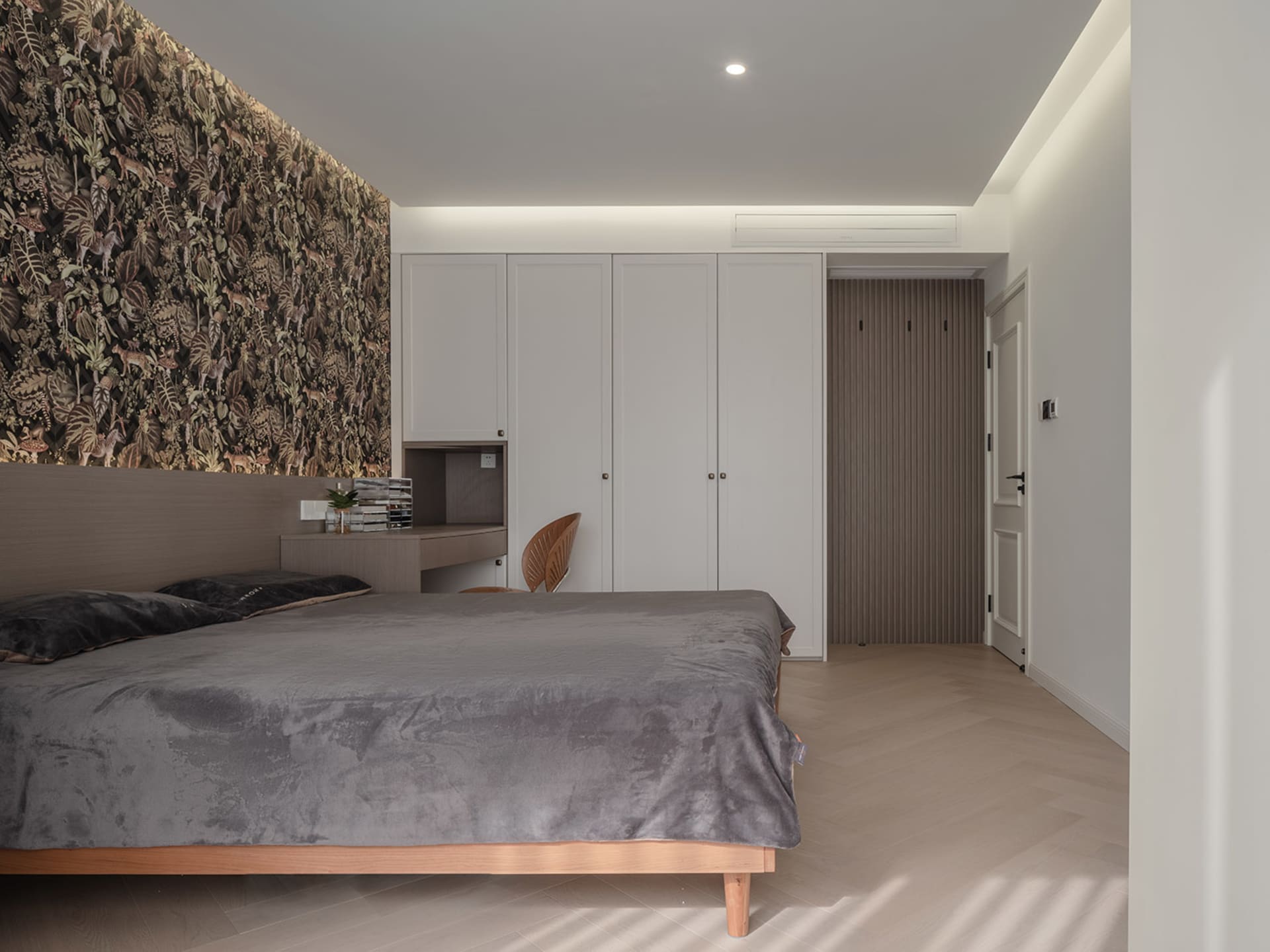 A modern bedroom featuring wooden furniture, a gray bedspread, and a natural wood floor.