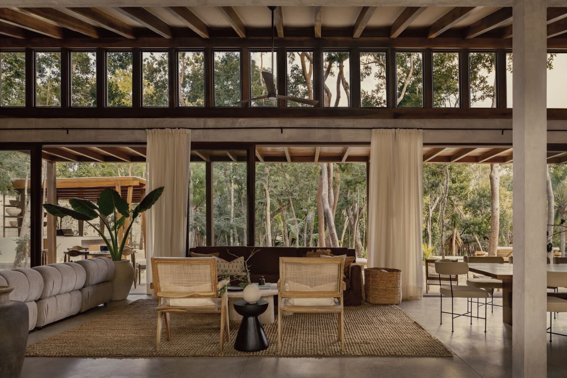 A modern living room with wooden furniture, large windows, and a view of the forest.