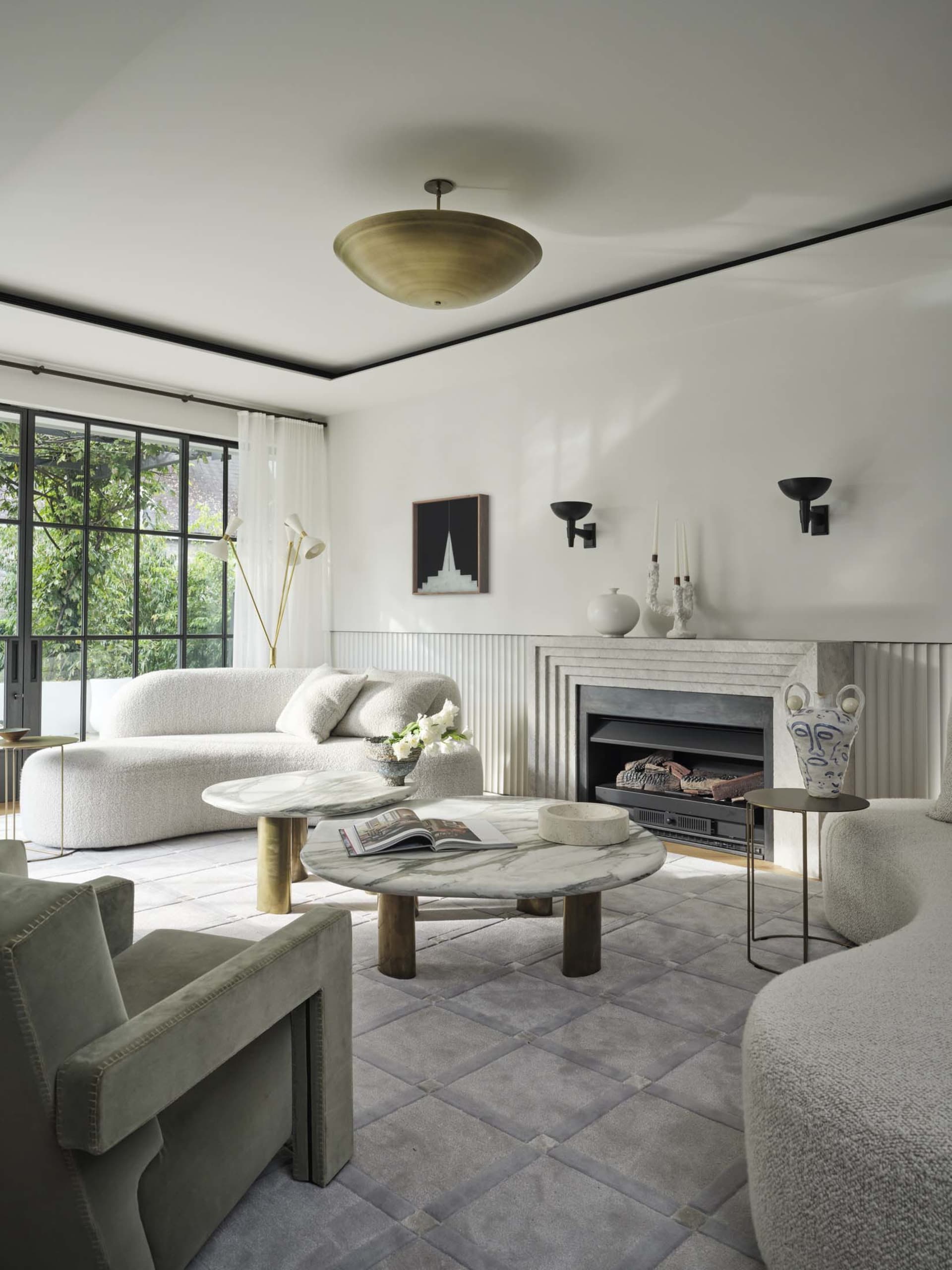 Minimalist living room featuring marble tables, a plush sofa, and a cozy fireplace, with a view of the outdoors through large