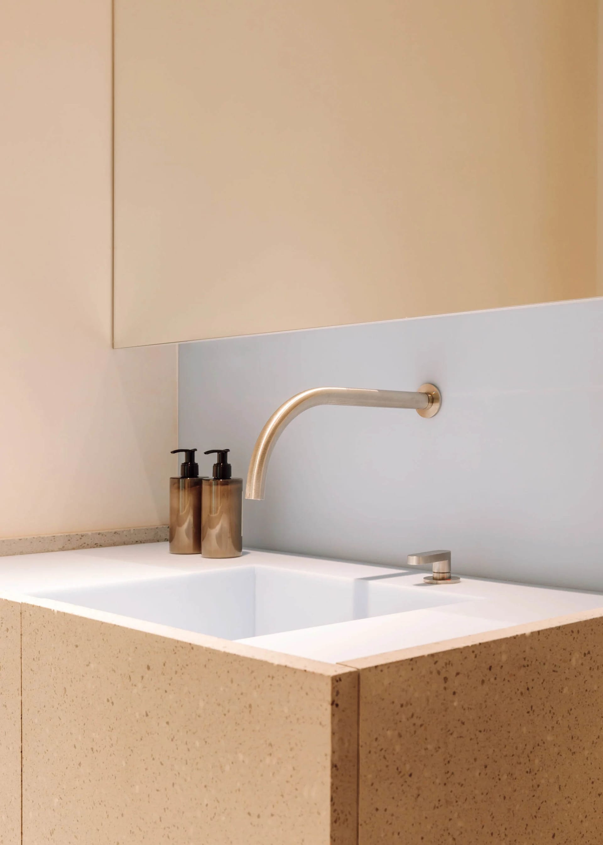 A minimalist bathroom with a white concrete sink, a brushed stainless steel faucet, and black liquid soap dispensers.
