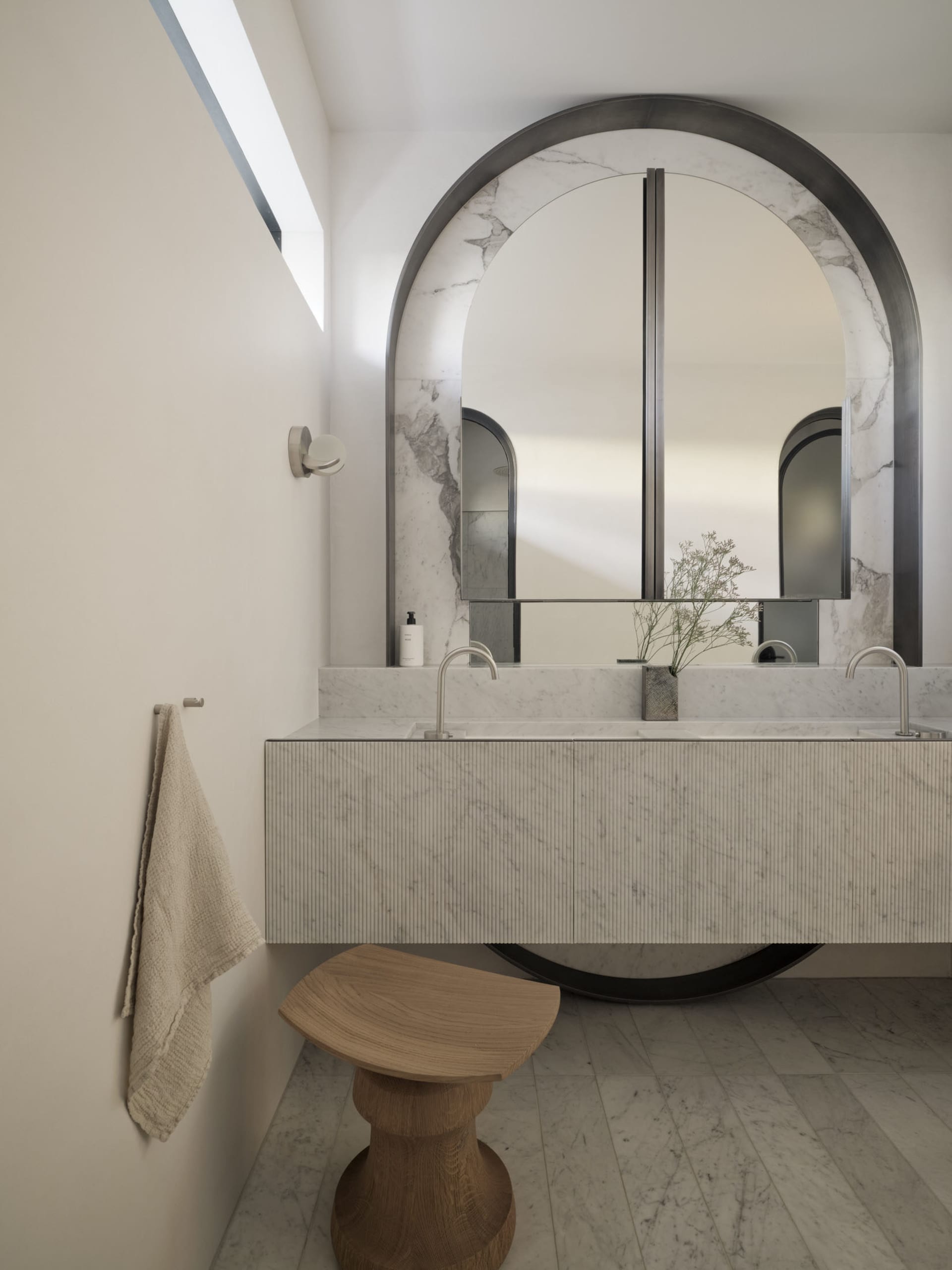Modern bathroom with marble walls, a floating vanity, and an arched mirror.