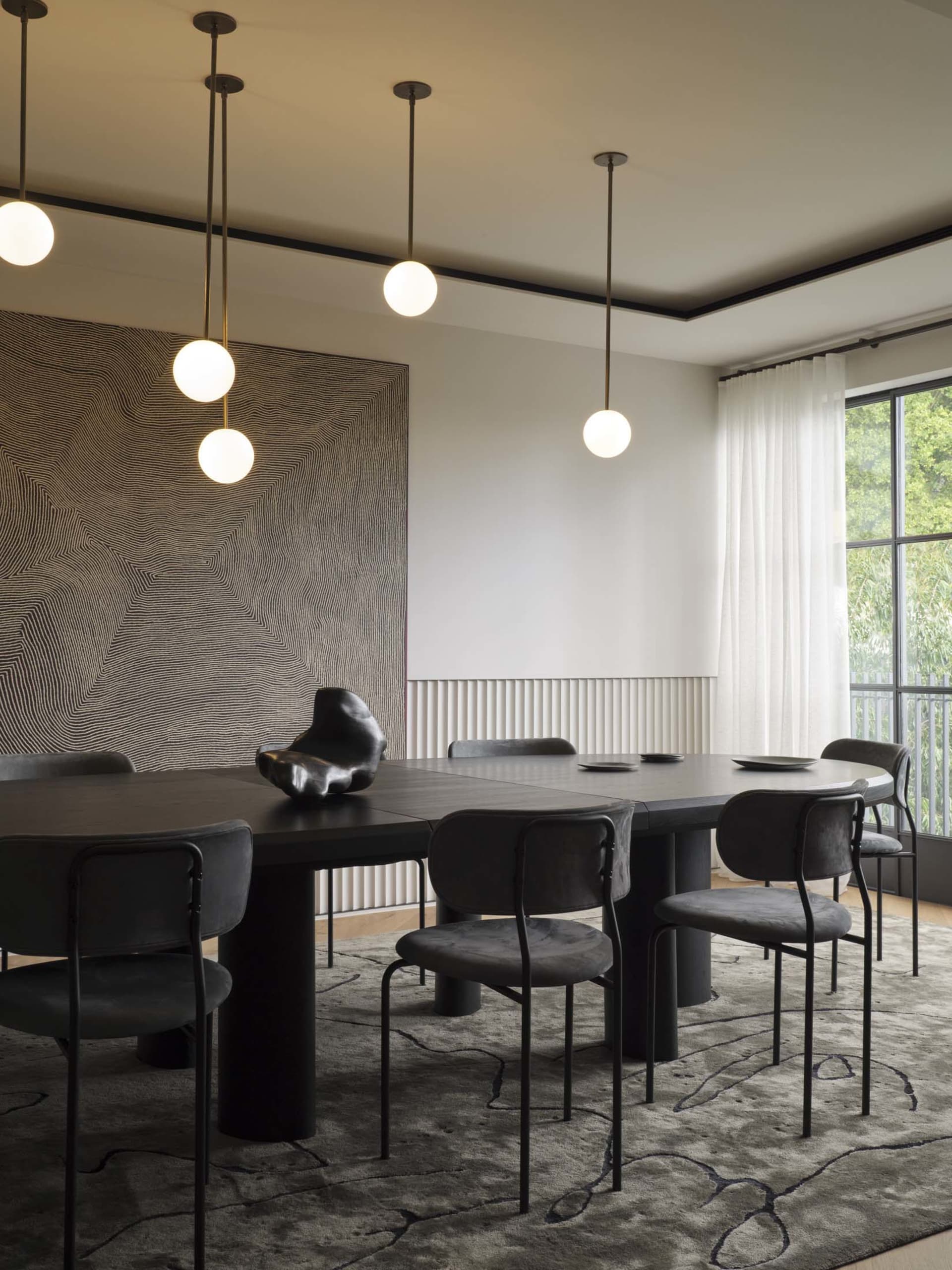 Modern dining room featuring a large round table with dark wood and metal chairs, white pendant lights, and a black and white