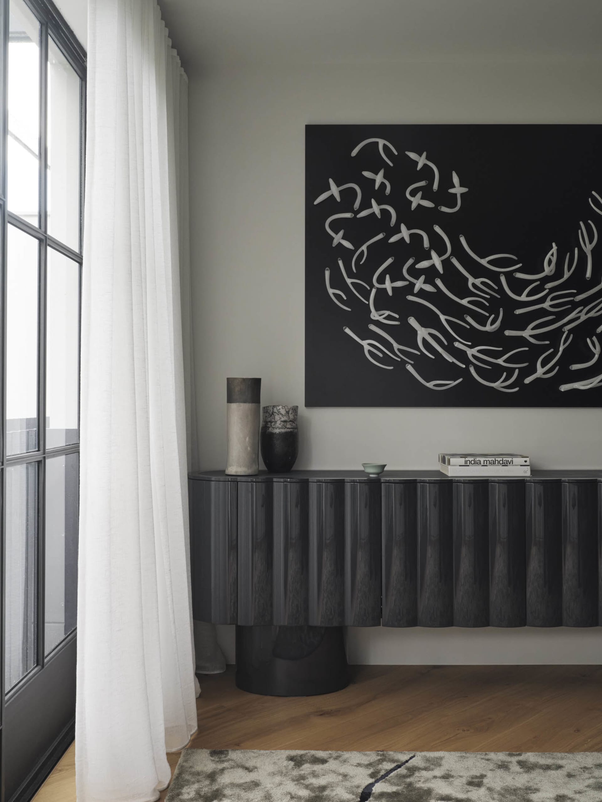 A modern interior design featuring a black console table with a textured surface and three decorative items on top, including