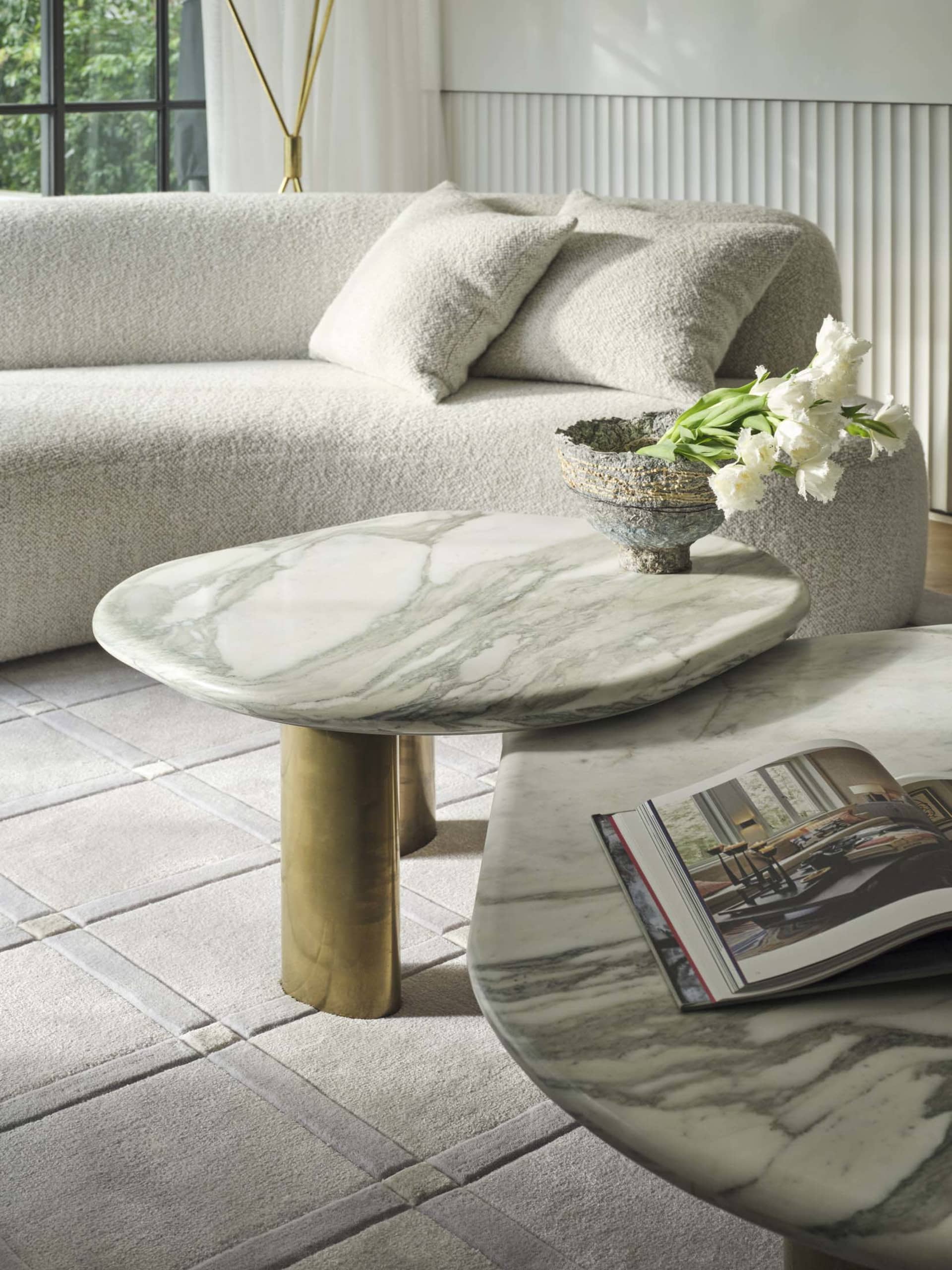 A modern living room featuring a cozy sofa with white and beige cushions, accompanied by two marble coffee tables with a bras