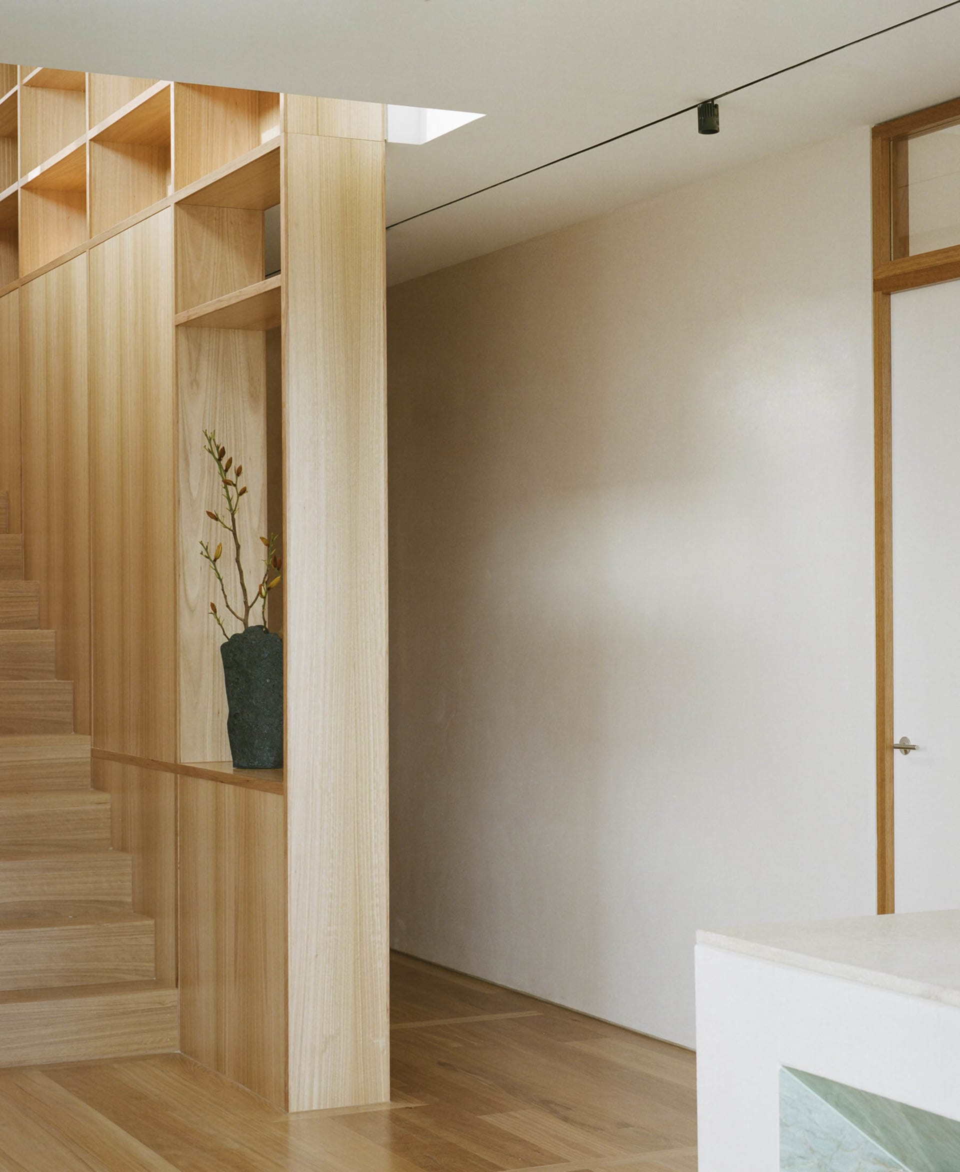 A minimalist staircase with a built-in bookshelf displaying a vase with flowers.
