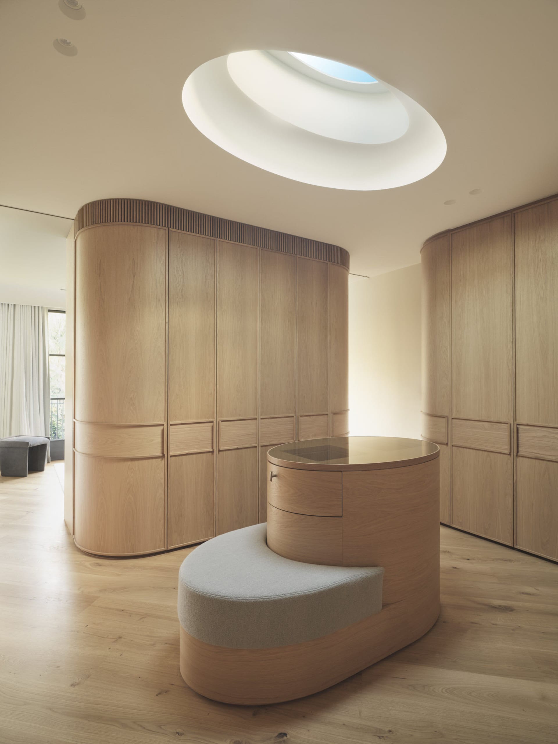 Minimalist wooden wardrobe room featuring a round glass-topped table and a curved skylight on the ceiling.