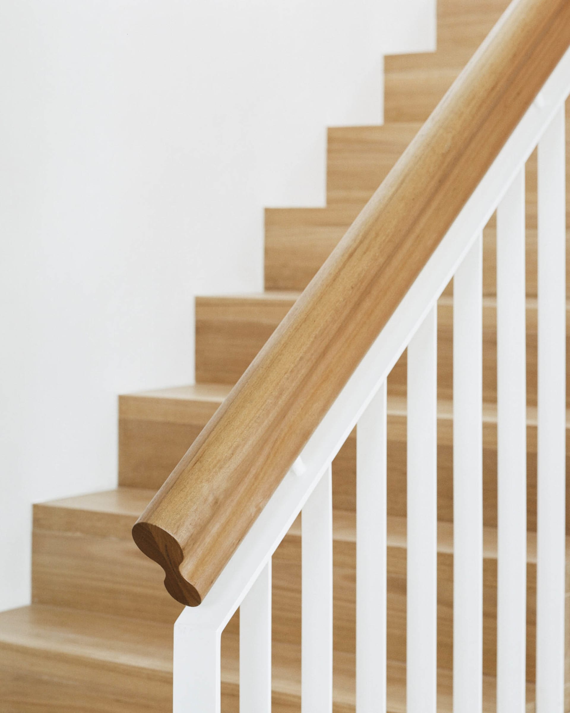 A modern staircase with a white handrail and wooden steps.