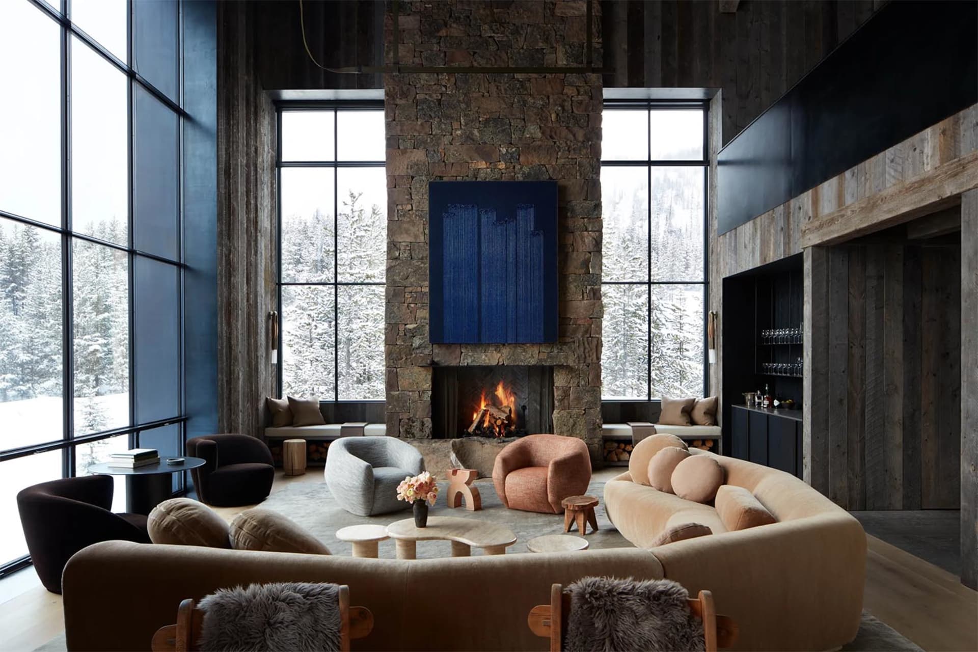 A modern living room with a stone fireplace, large windows, and minimalist furniture.