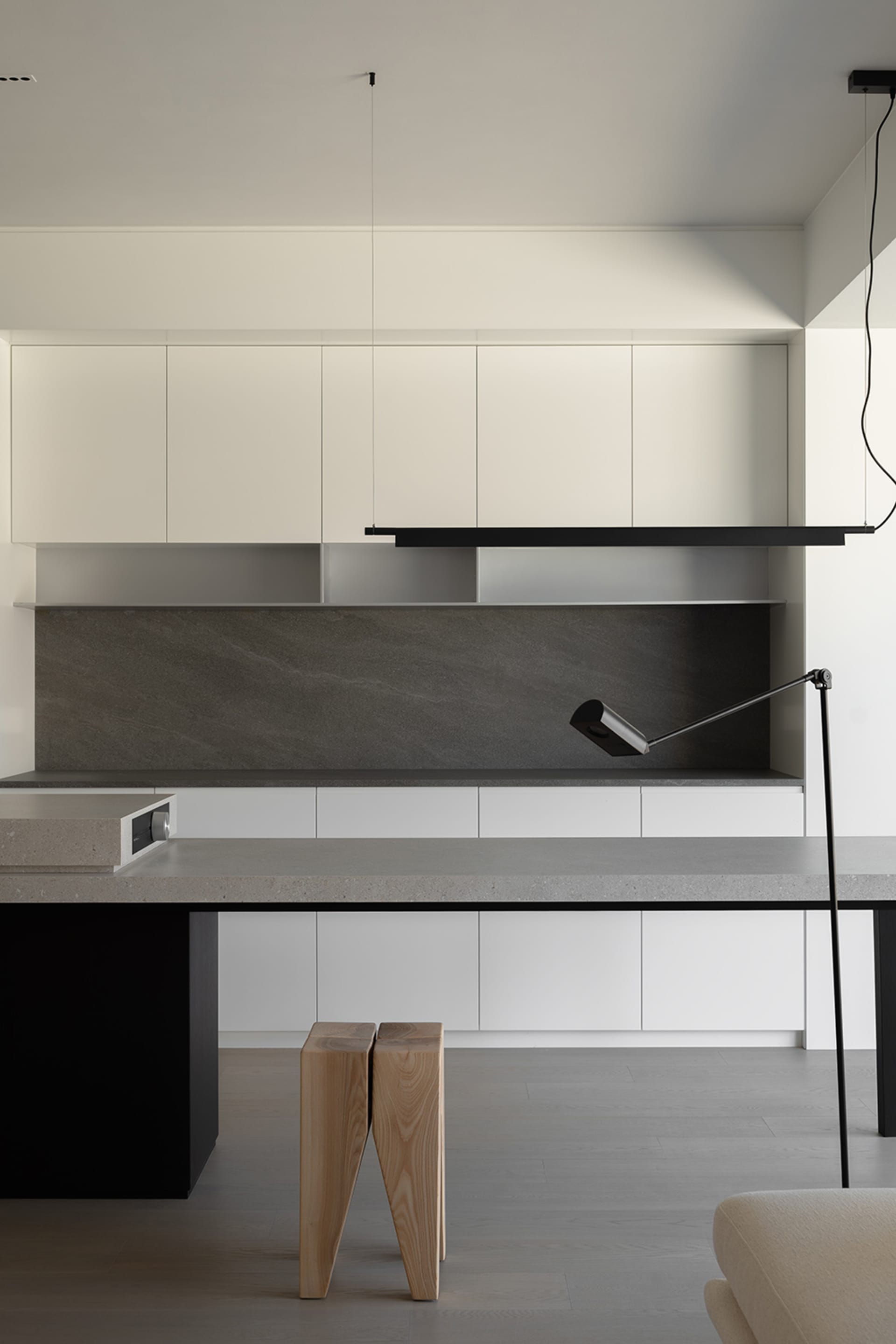 A modern minimalist kitchen with white cabinets, a concrete countertop, and wooden stools.