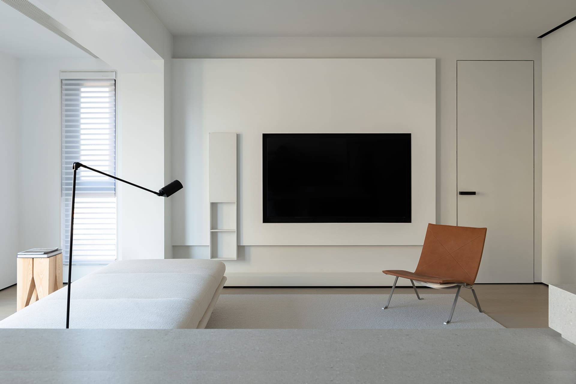 一間現代簡約客廳，配有白色沙發、棕色皮革椅、黑色可調式落地燈，以及大型螢幕電視