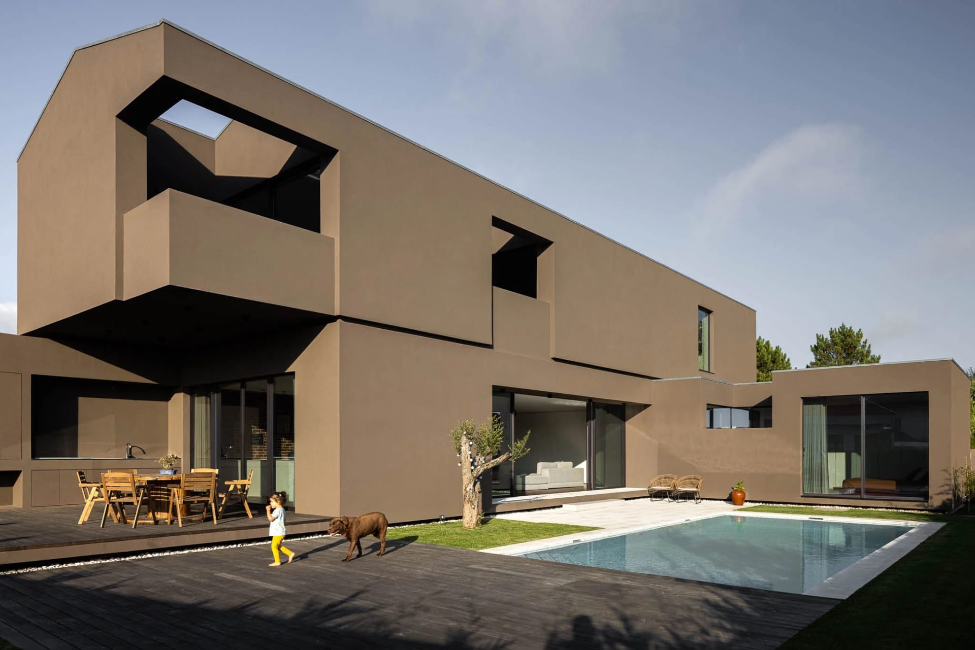 Modern residential home featuring concrete architecture with a swimming pool and a child walking with a dog.