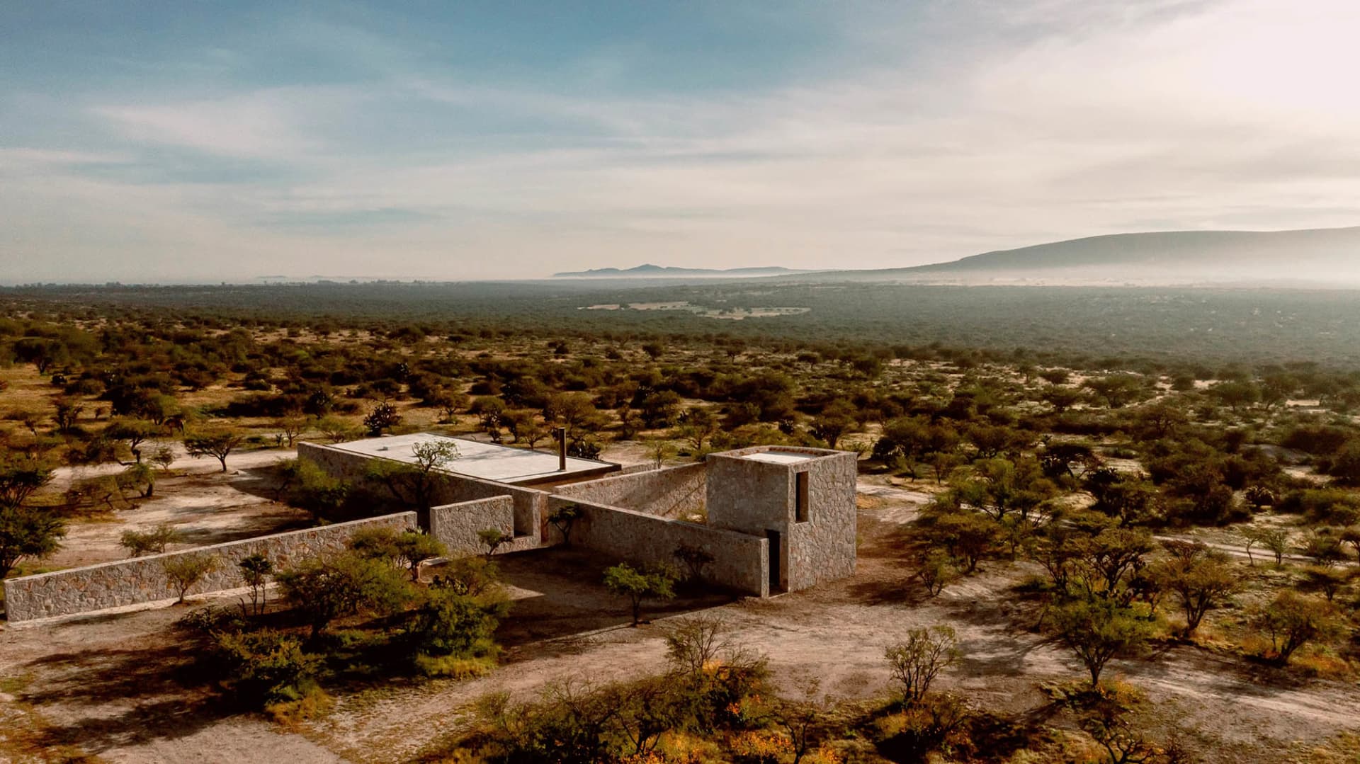 A modern stone house surrounded by trees in a desert landscape.