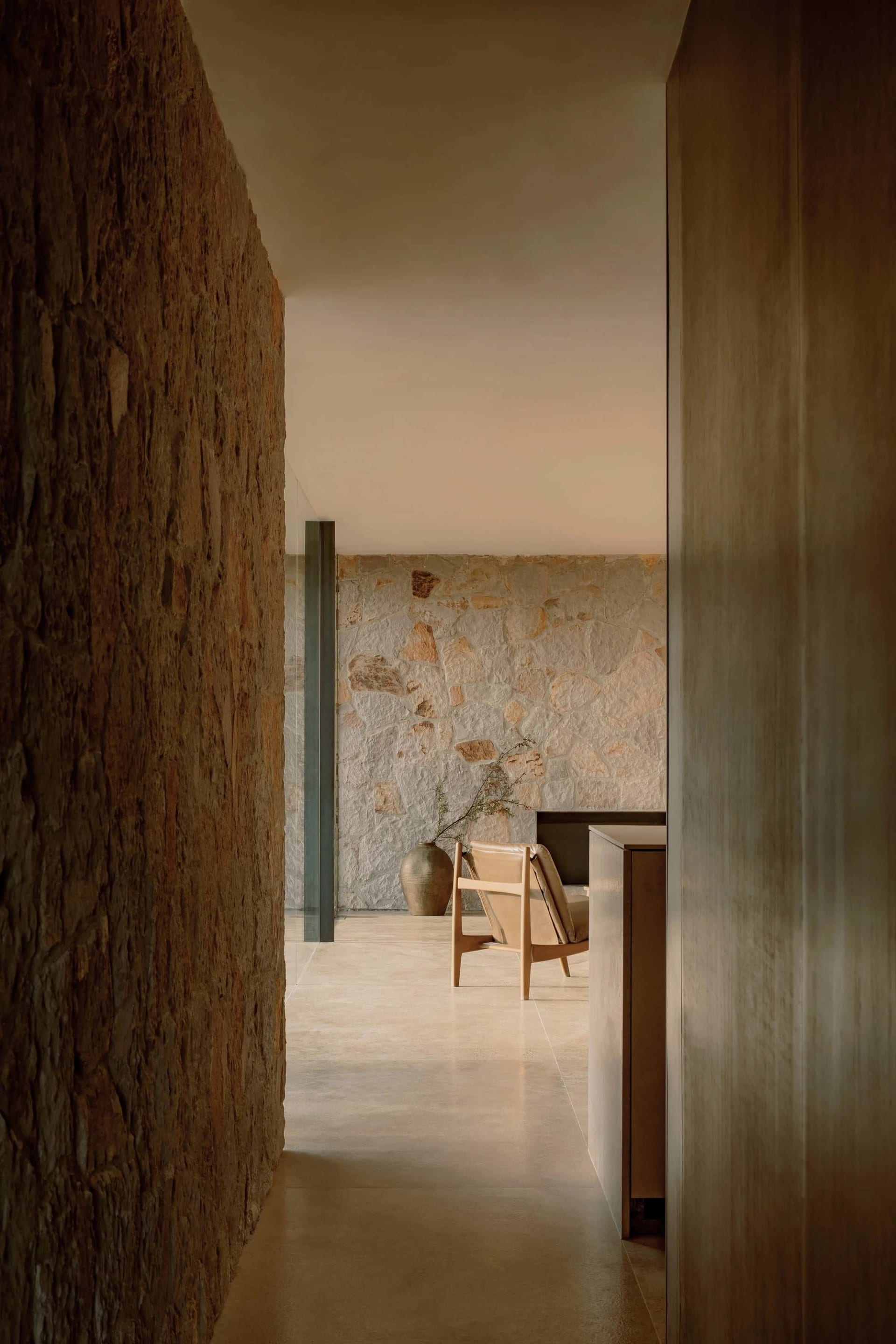 A minimalist living room with concrete walls, a wooden armchair, and a vase with green branches.