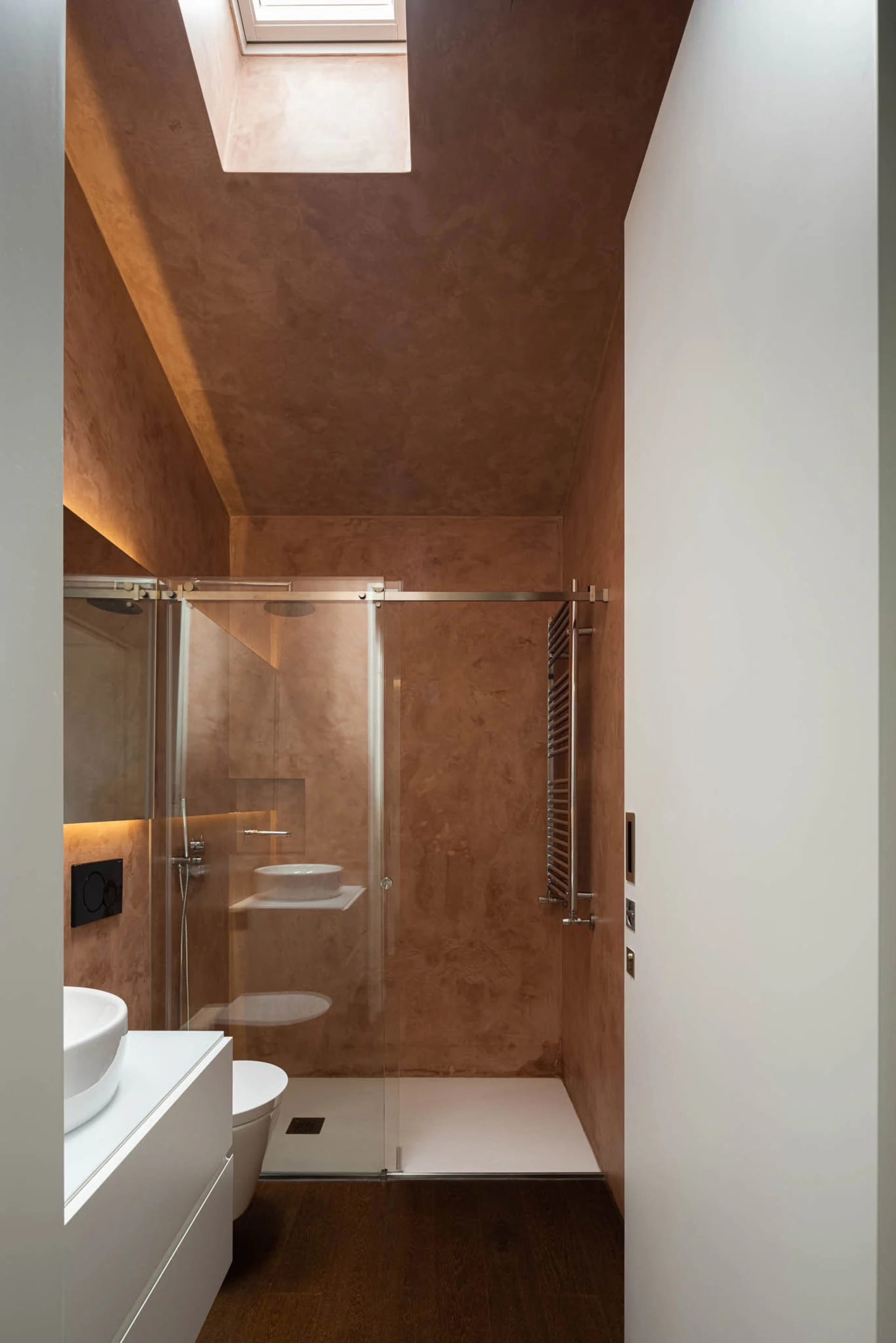 A modern bathroom features a concrete shower enclosure with a glass sliding door, a white floating vanity sink, and a skyligh
