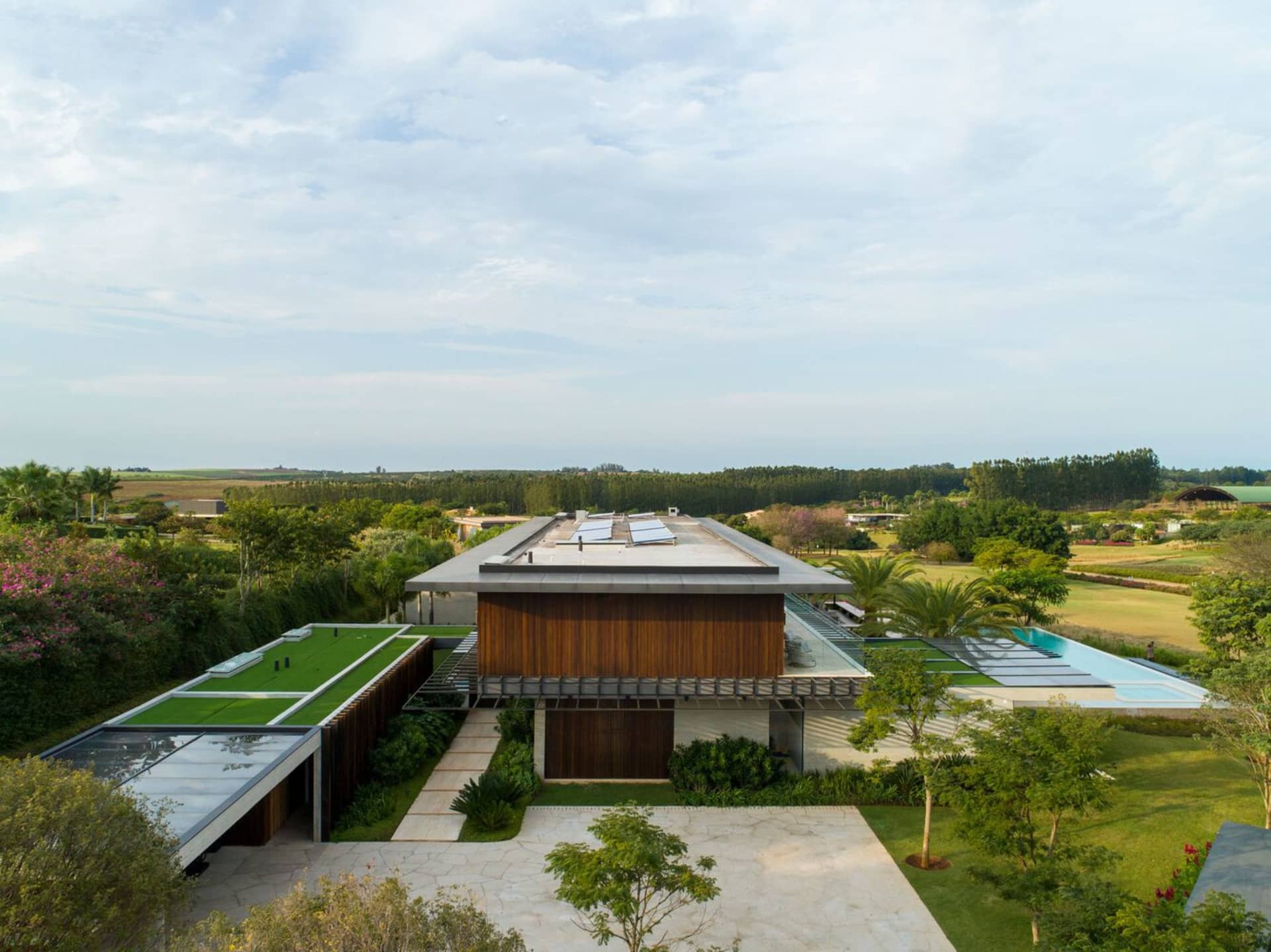 Modern residential exterior featuring large glass windows, wooden accents, and lush greenery.