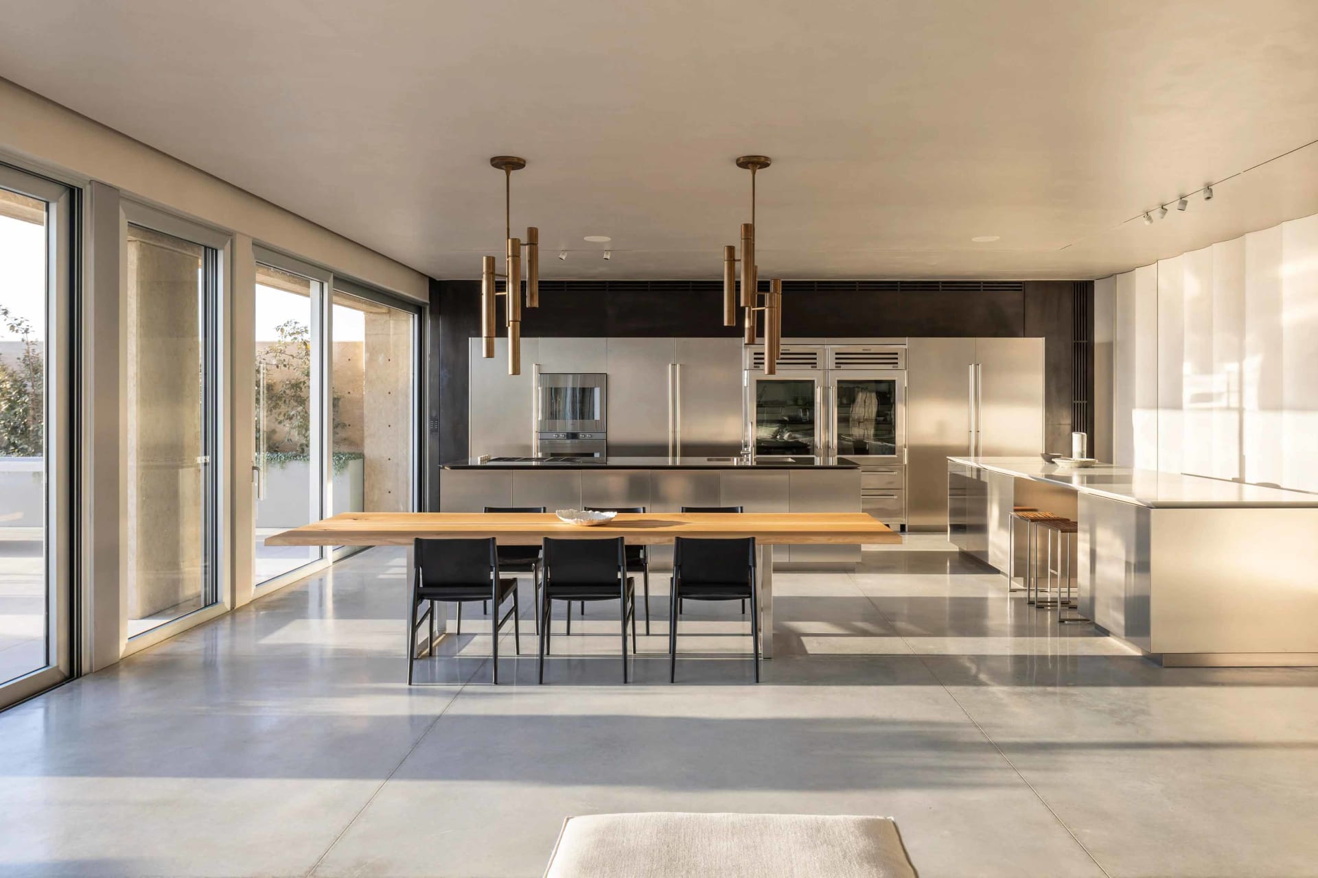 A modern residential kitchen featuring stainless steel cabinets and countertops, with a wooden dining table and black chairs.