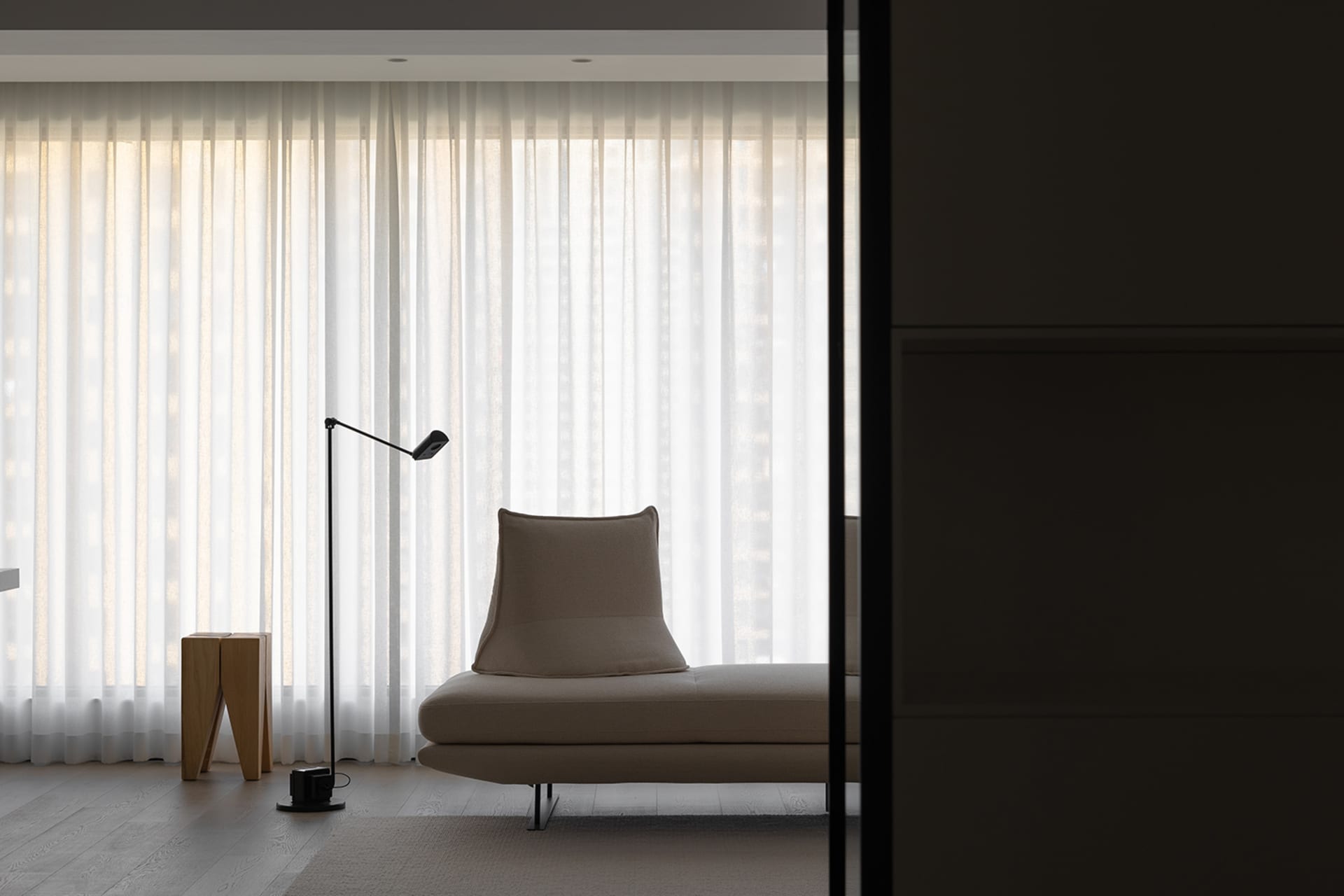 Modern minimalist living room with a beige upholstered lounge chair, a black floor lamp, and sheer white curtains.
