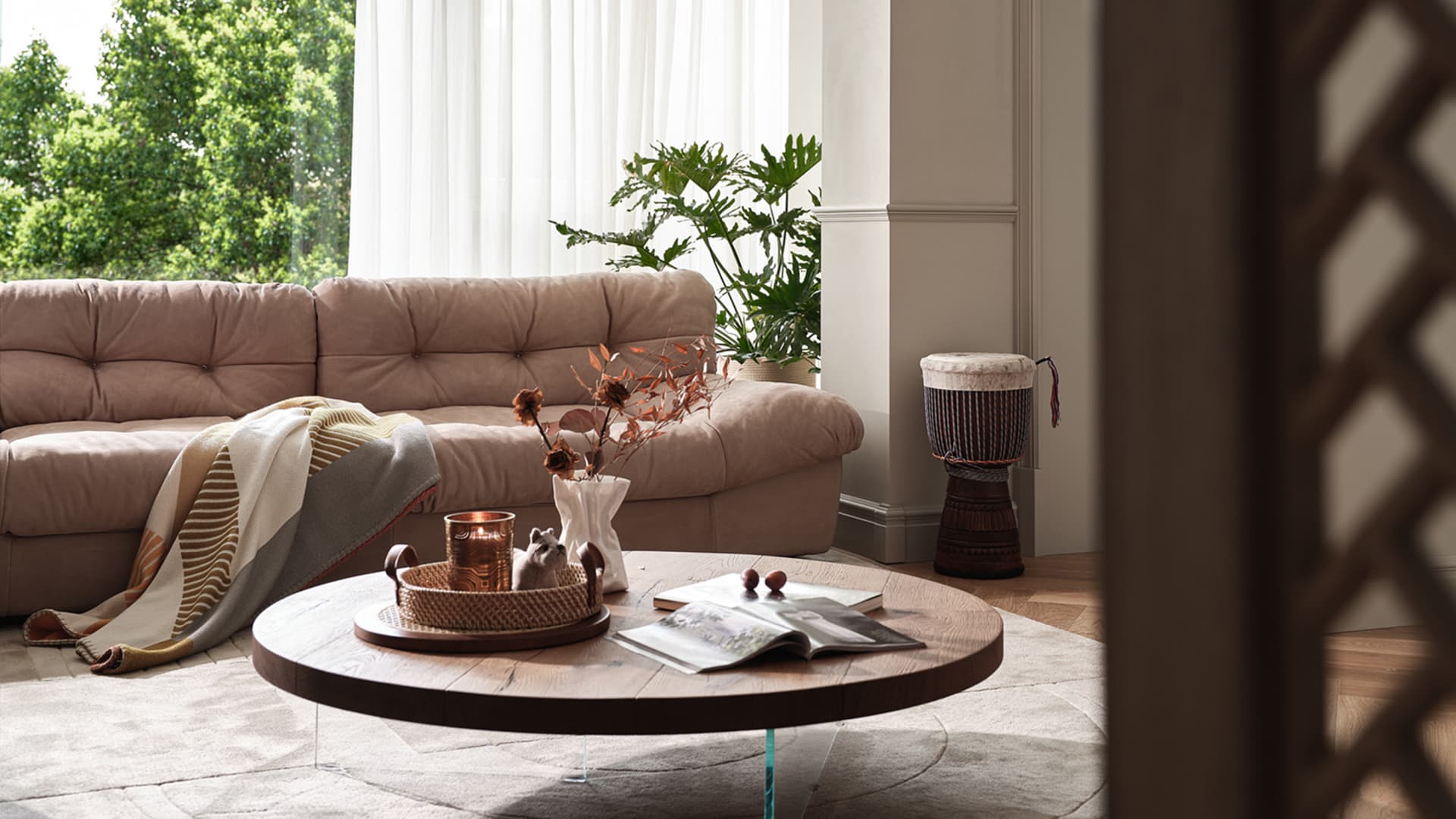 A modern living room with a round wooden coffee table, a beige leather sofa, and a plant in a white vase.
