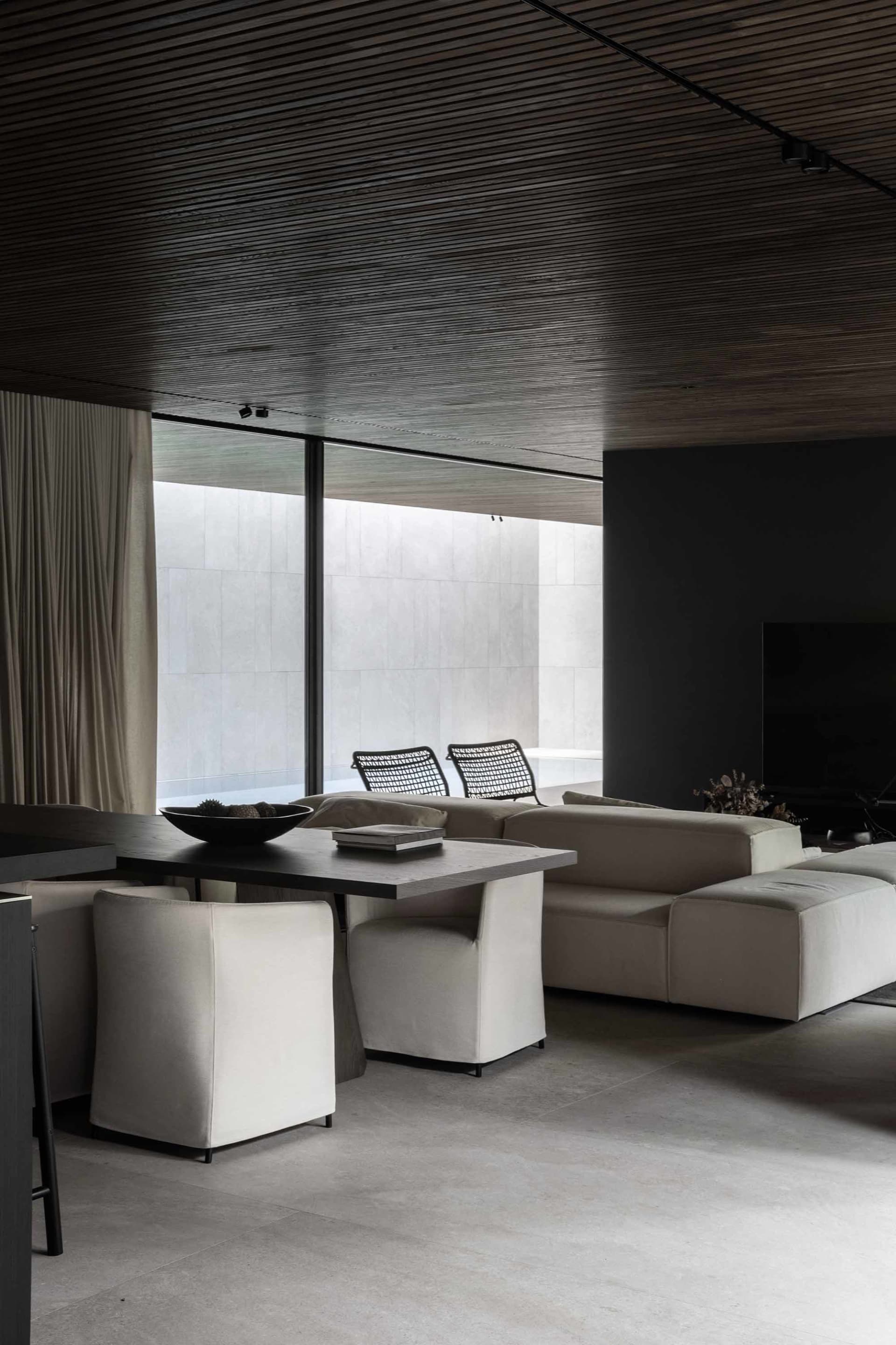 A modern minimalist living room with a concrete floor, a large window, white sofas, and a dining table.