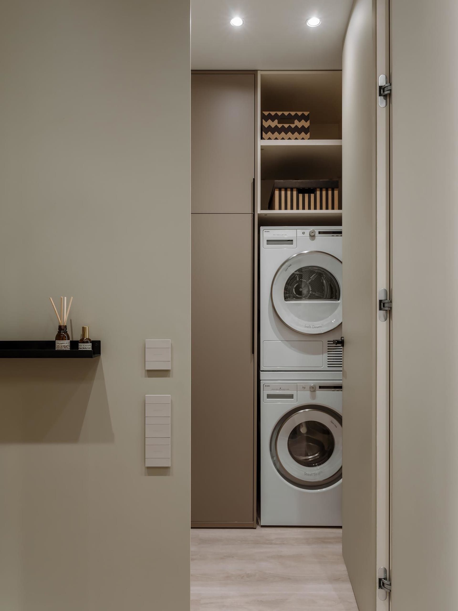 A modern, neutral-colored laundry room with stacked washer and dryer appliances.