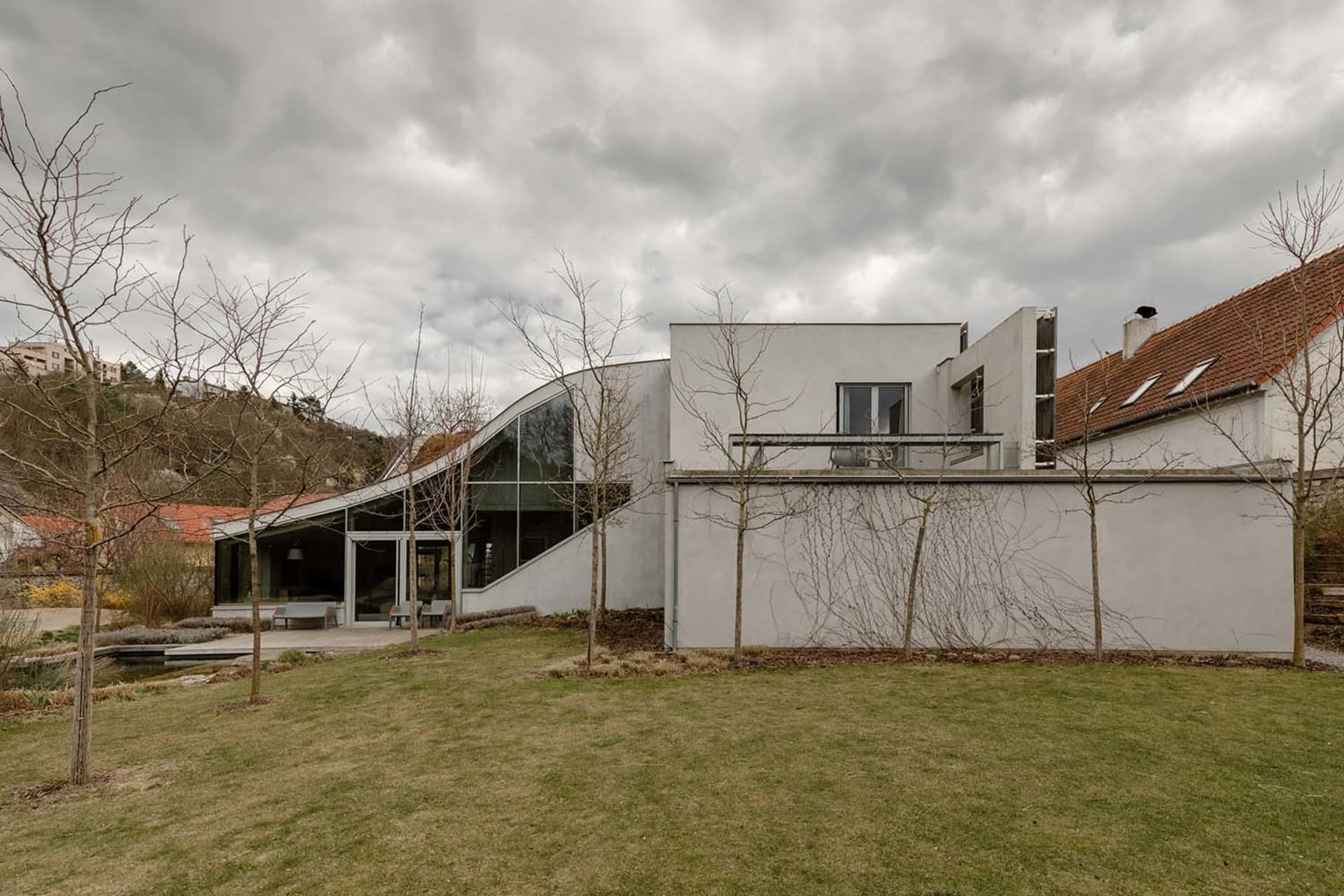 A contemporary residential home featuring modern architecture, concrete walls, glass windows, and a sloping green roof.