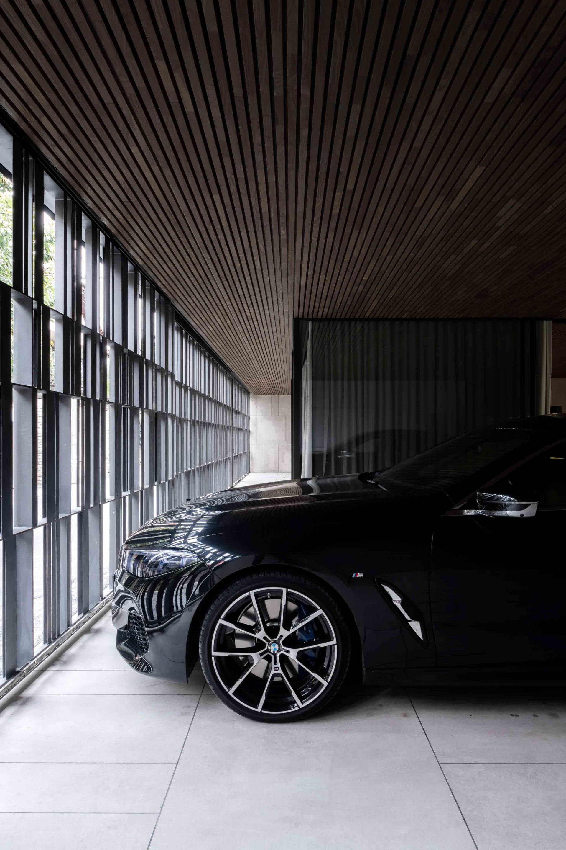Black car parked in a modern garage, with wooden slats and large windows.