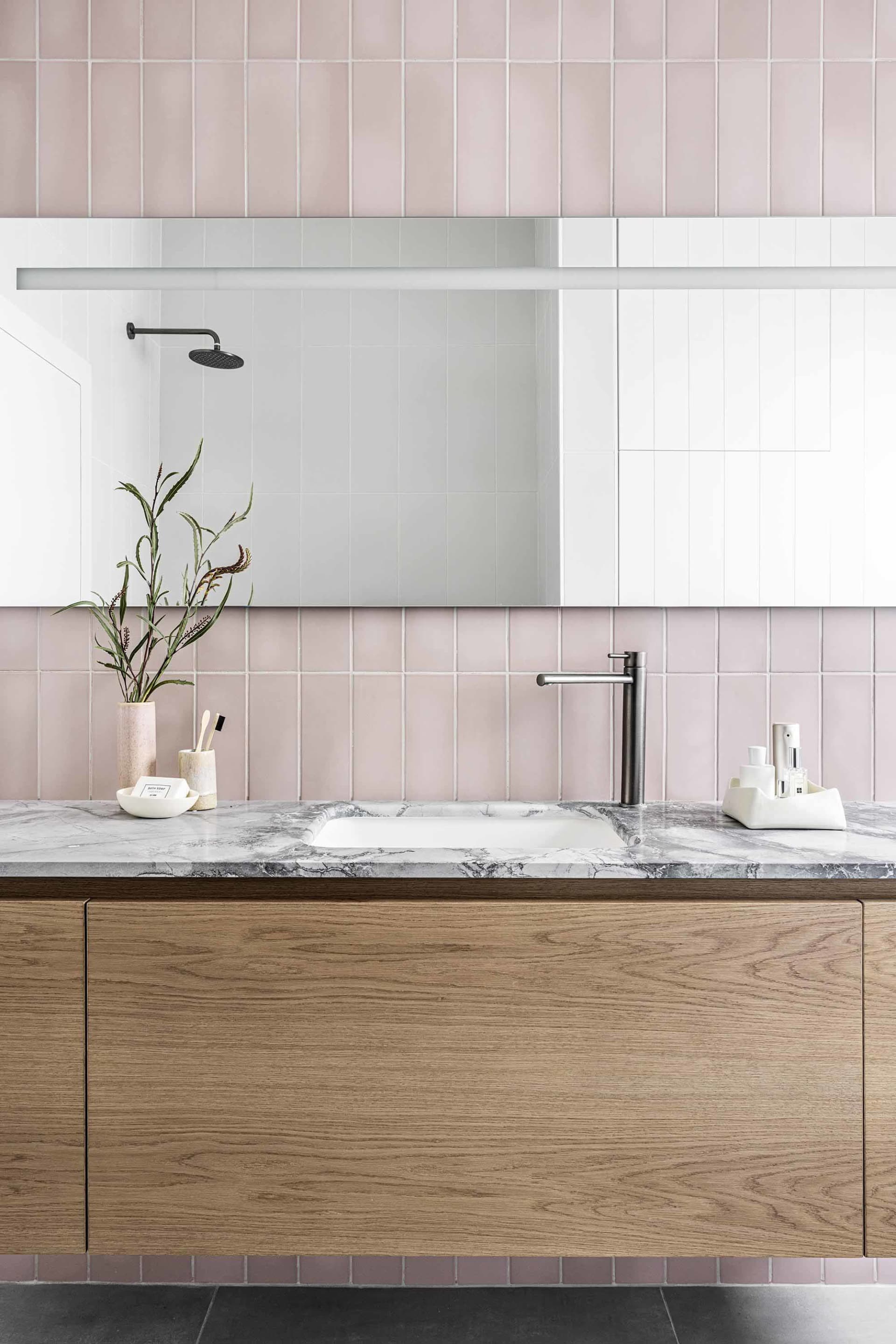 A minimalist bathroom with ceramic tiles features a vanity with a marble countertop, a wooden cabinet, a white sink, a mirror