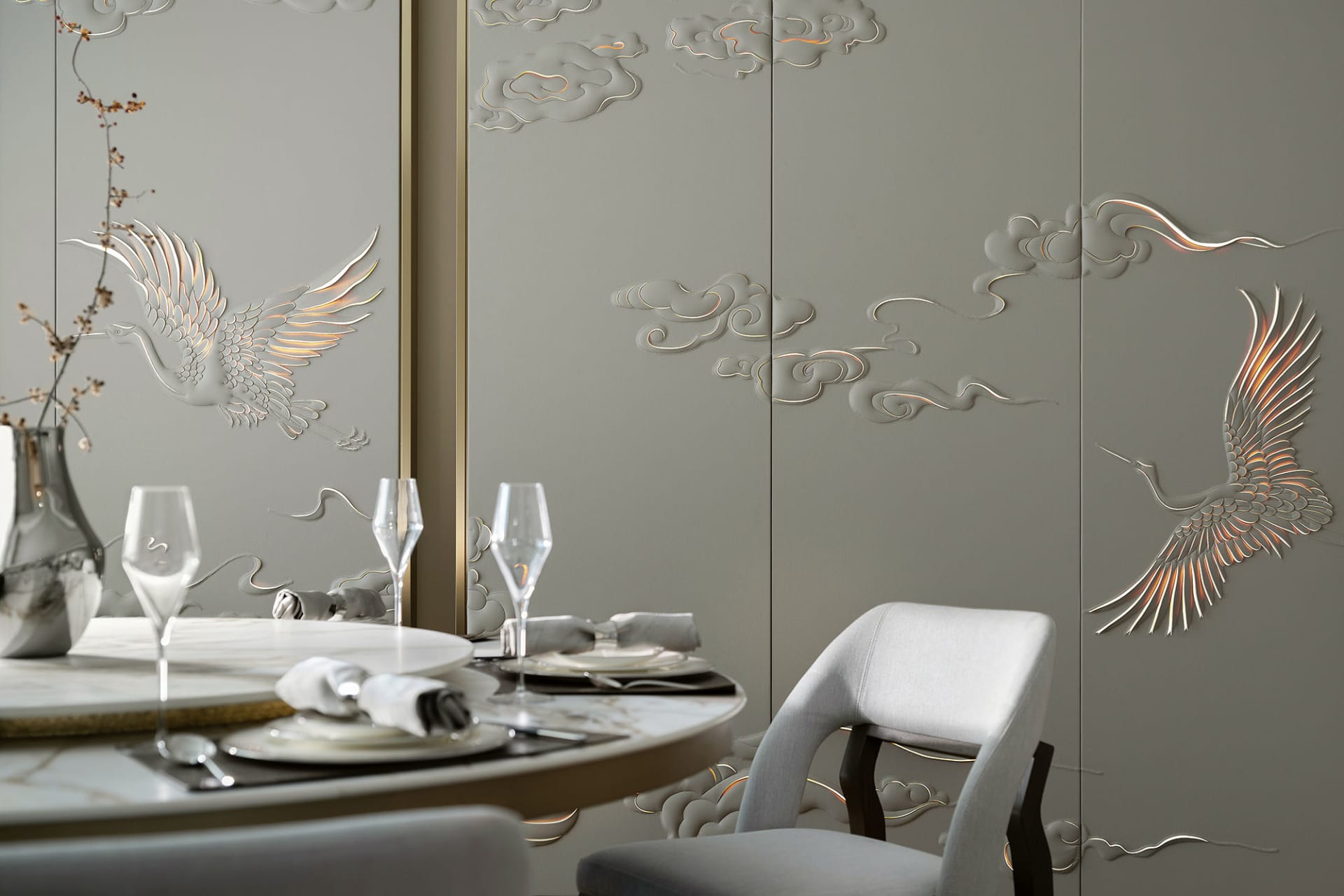 A modern dining room featuring metallic texture wall panels with bird and cloud motifs, table setting, and wine glasses.
