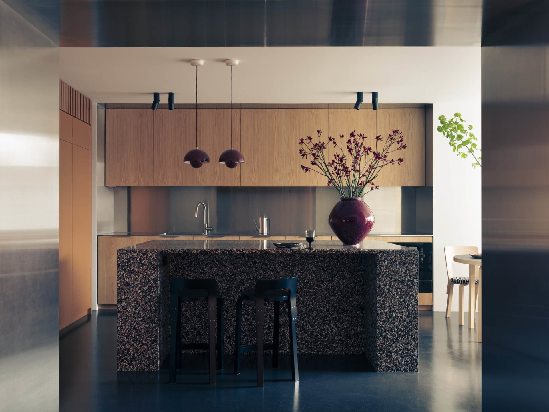 A modern kitchen with granite countertops and stools, featuring a vase of flowers and a sleek design.