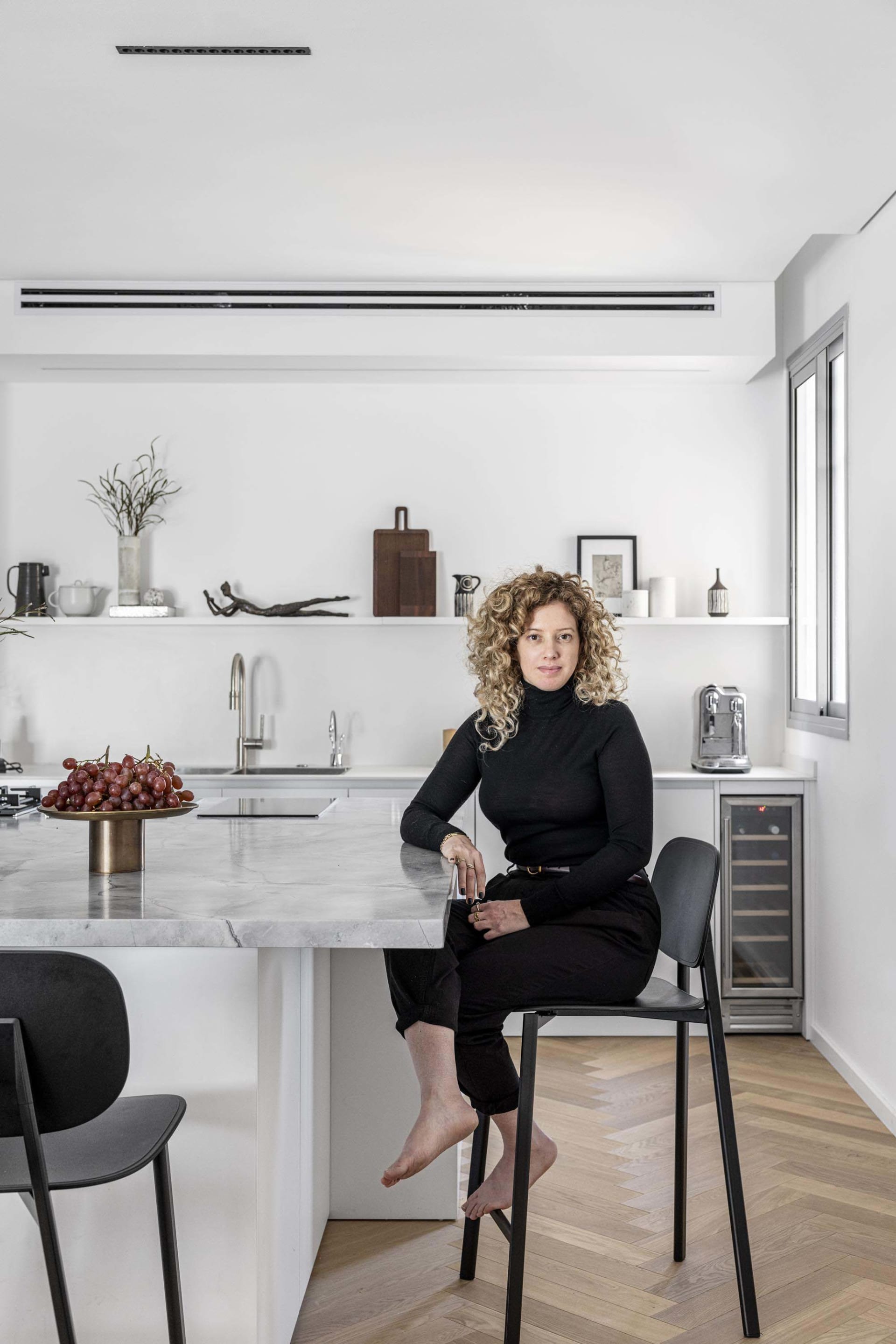 A minimalist kitchen featuring a marble countertop with a woman sitting on a stool.