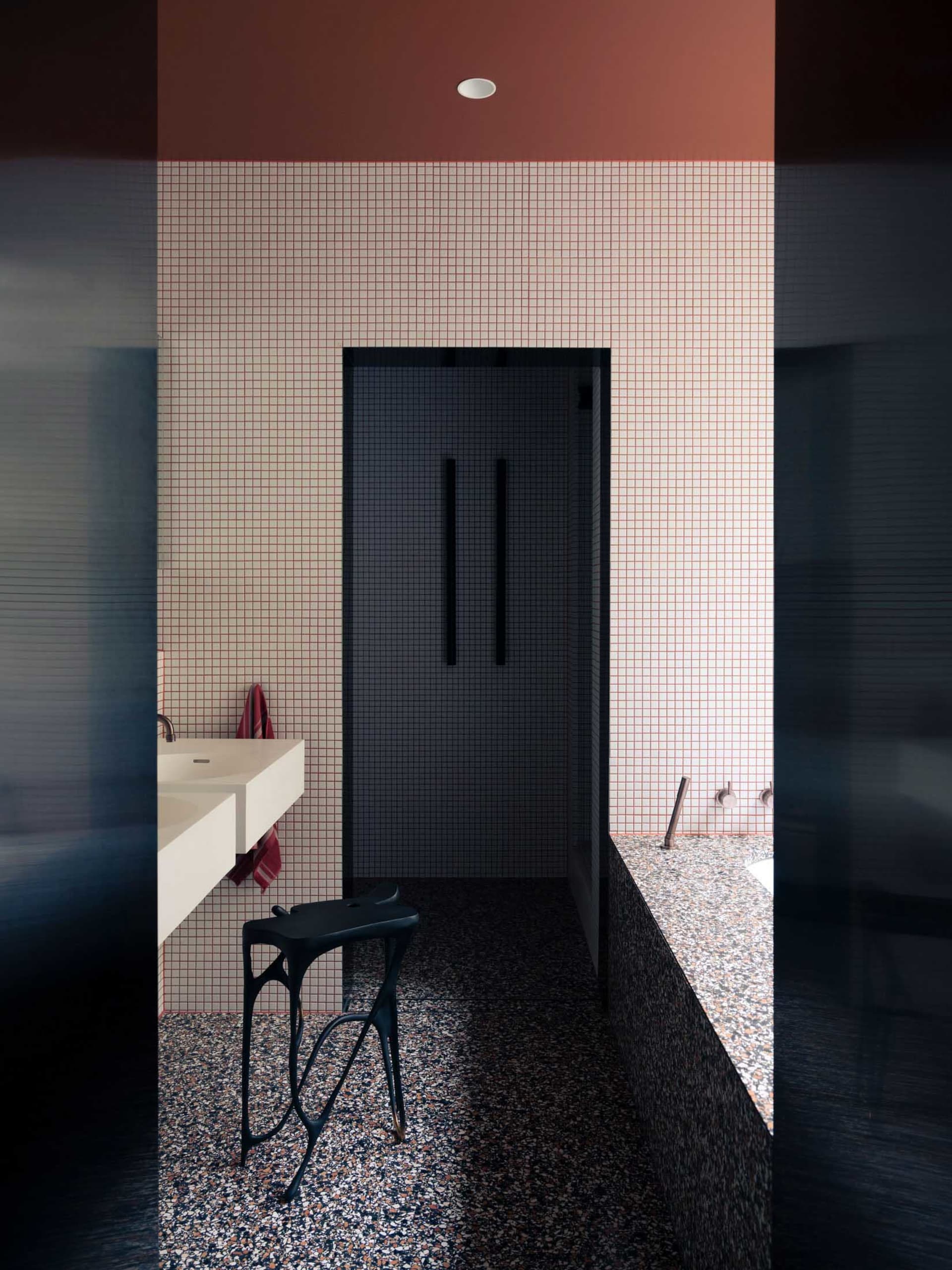 Modern bathroom with white and black mosaic floor tiles, white floating vanity, black metal stool, and a glass-enclosed showe