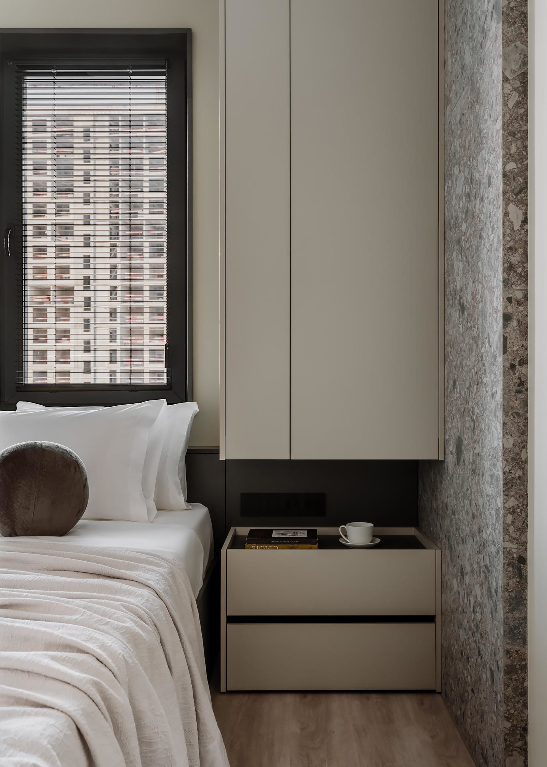 Minimalist bedroom featuring a bed with white bedding and a modern nightstand with a cup and books, set against a terrazzo wa
