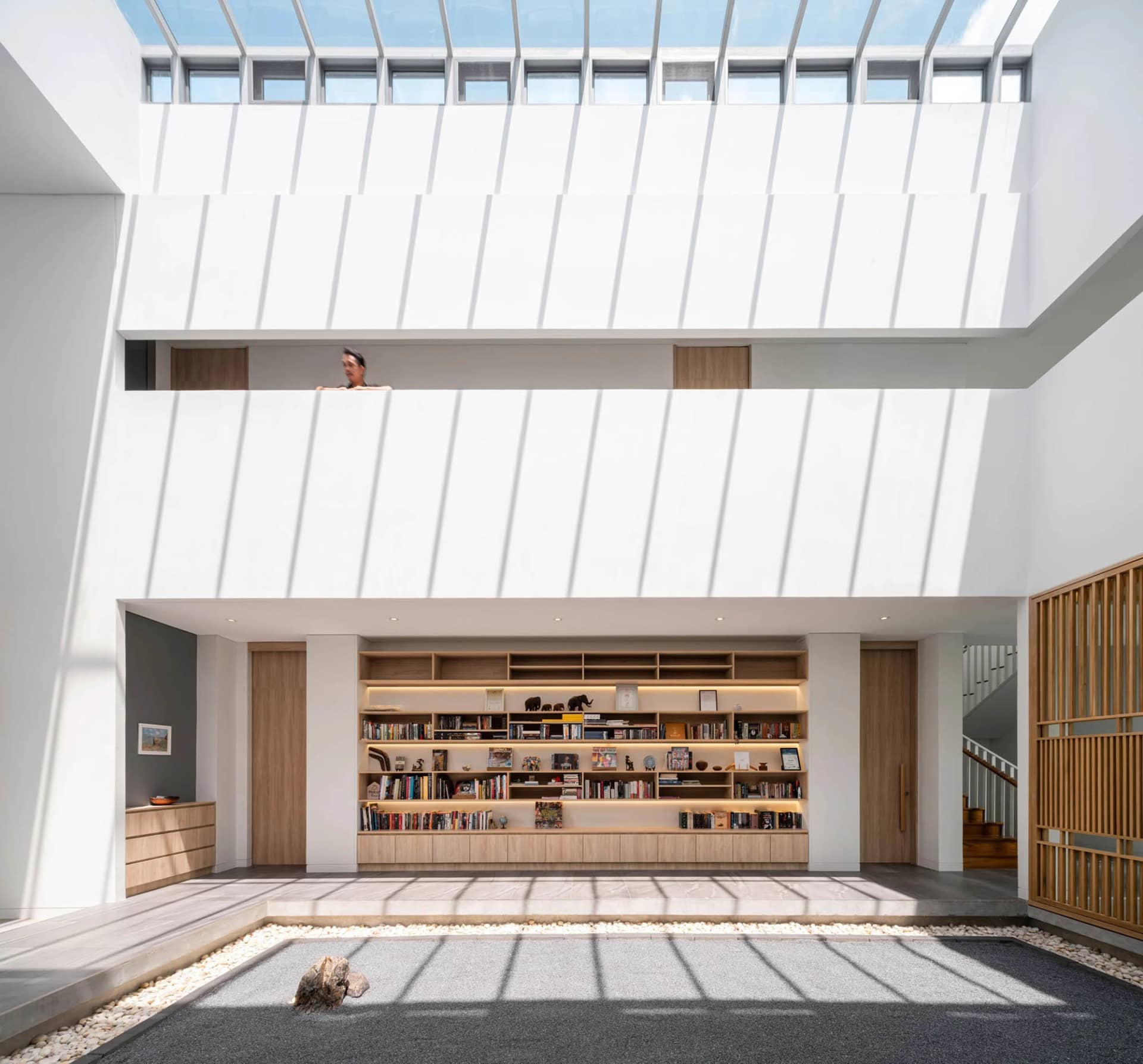 Modern minimalist living space featuring concrete and wooden elements with a central bookshelf and Zen garden.