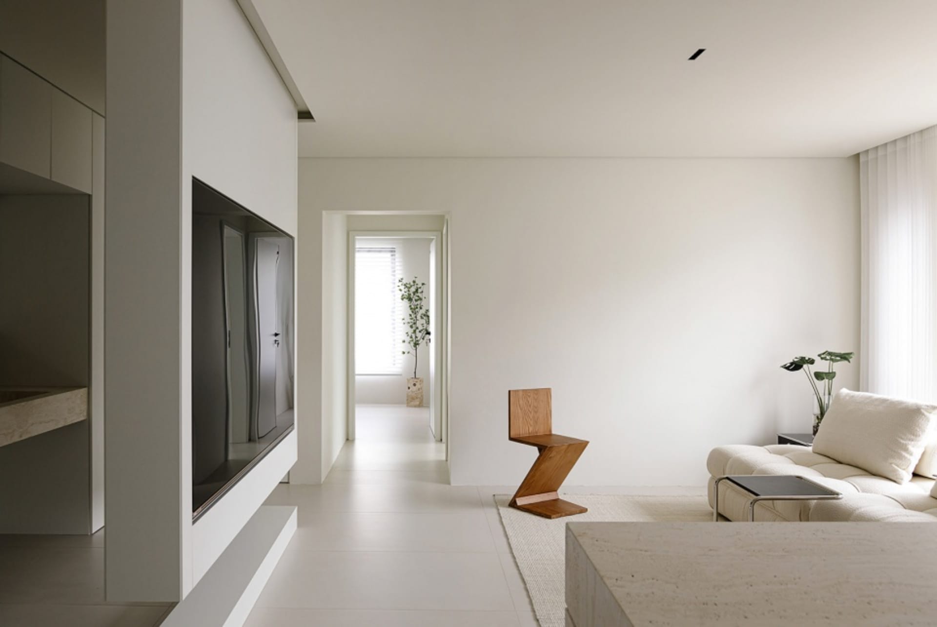 Modern minimalist living room featuring a white sofa, a sleek wooden chair, and a flat-screen TV mounted on a concrete wall.