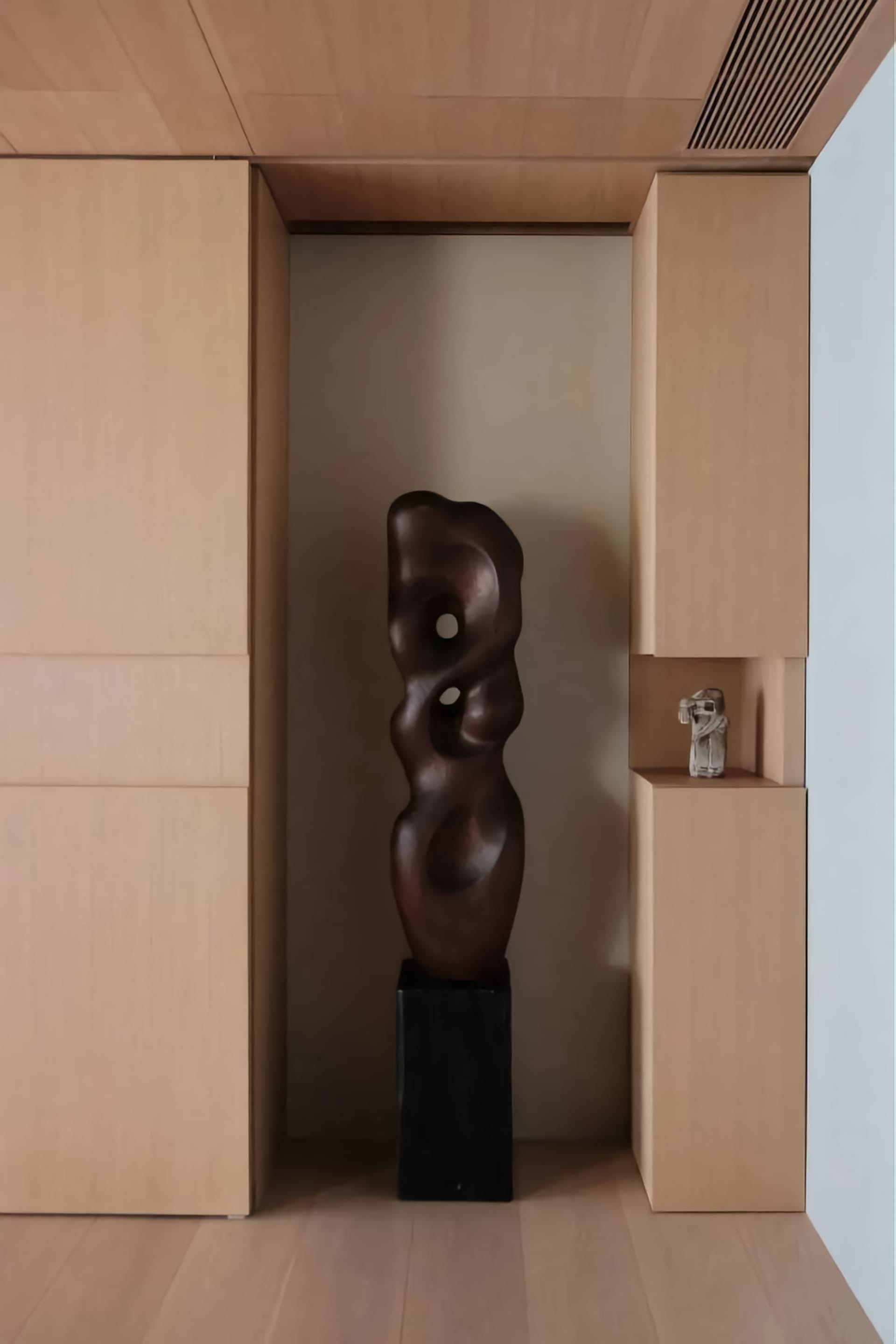 A tall, abstract wooden sculpture displayed between wooden cabinets in an interior setting.