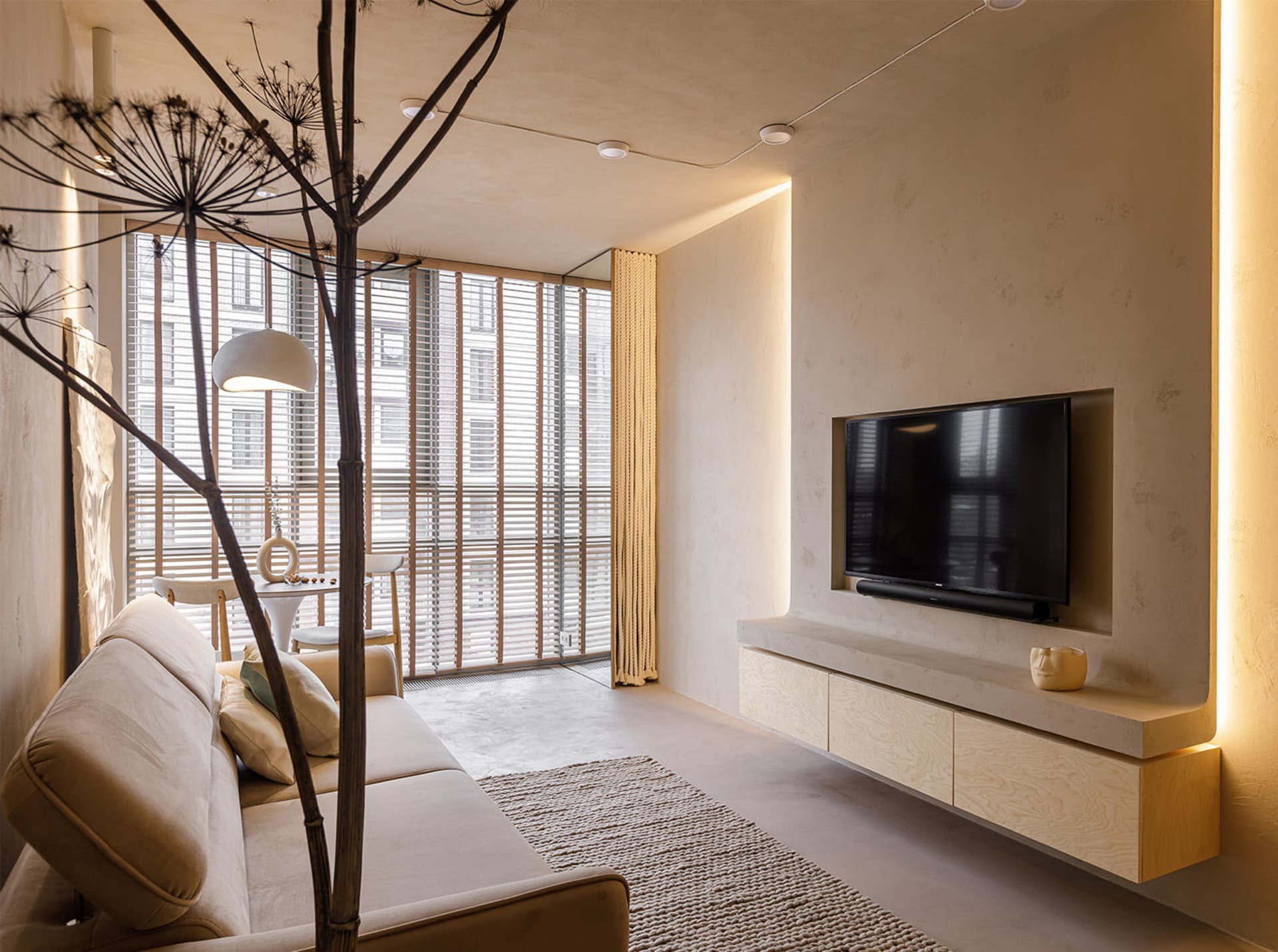 A minimalist living room with concrete flooring, wood furniture, and a floor lamp.