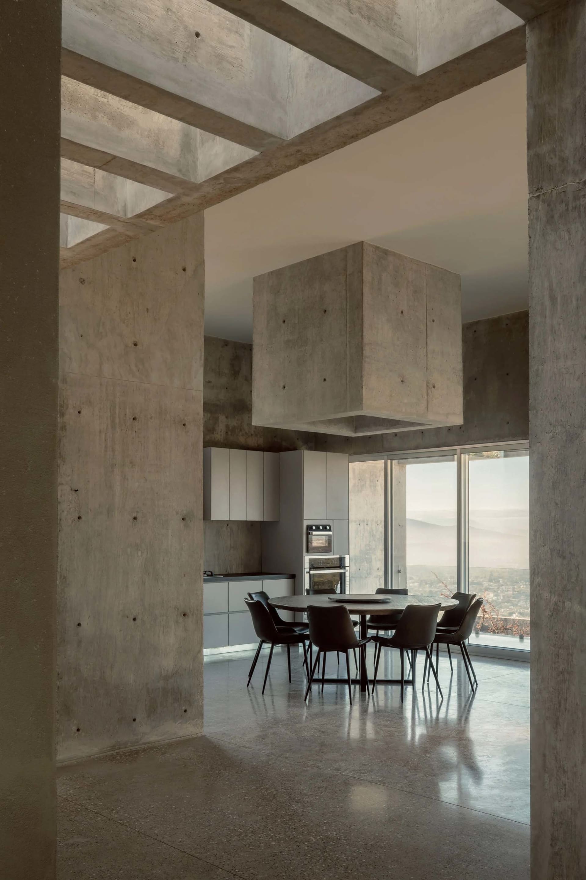 A modern industrial dining room with concrete walls, a suspended concrete structure, and a round dining table.