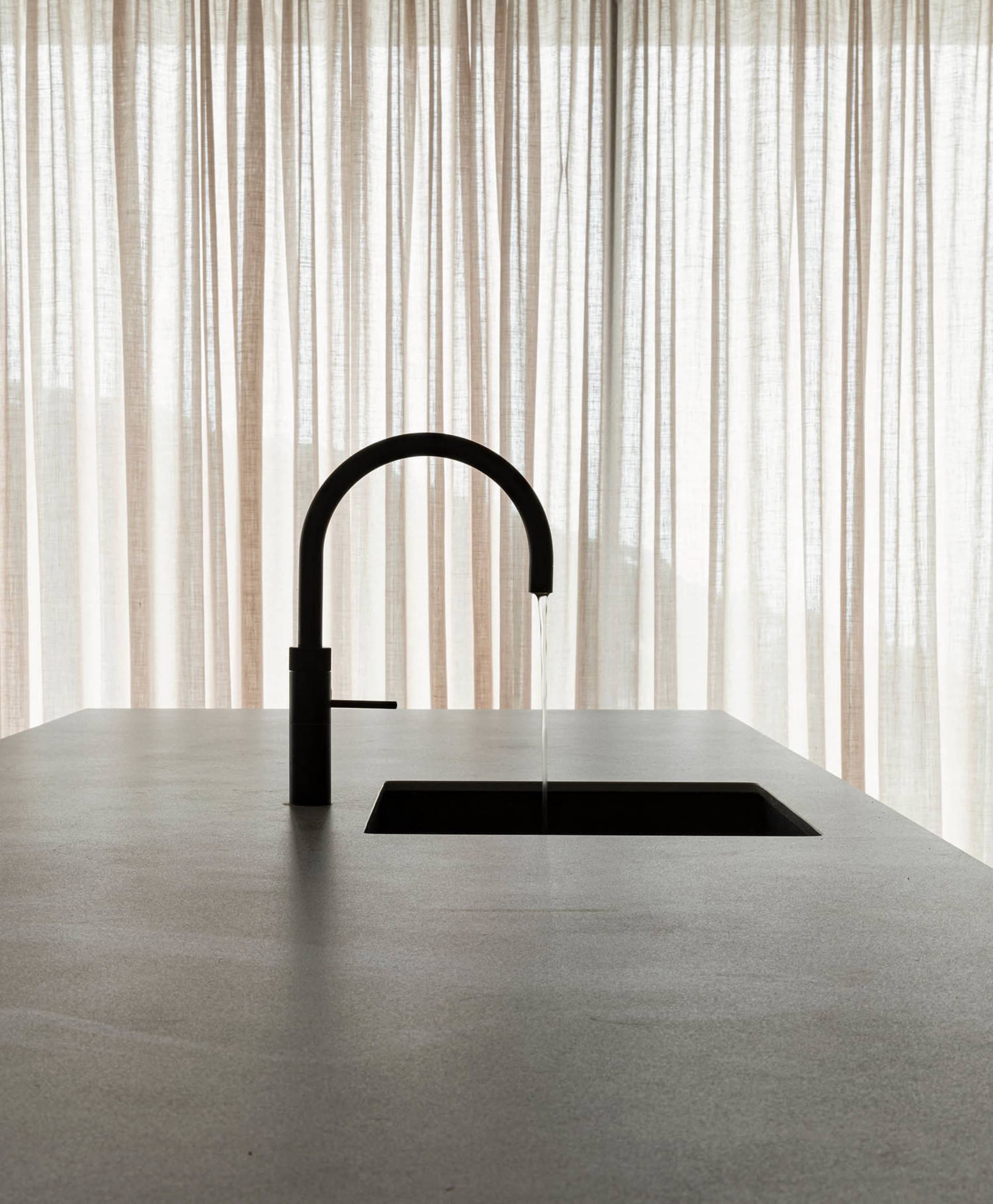 A minimalist modern kitchen featuring a concrete countertop and sink with a black faucet.