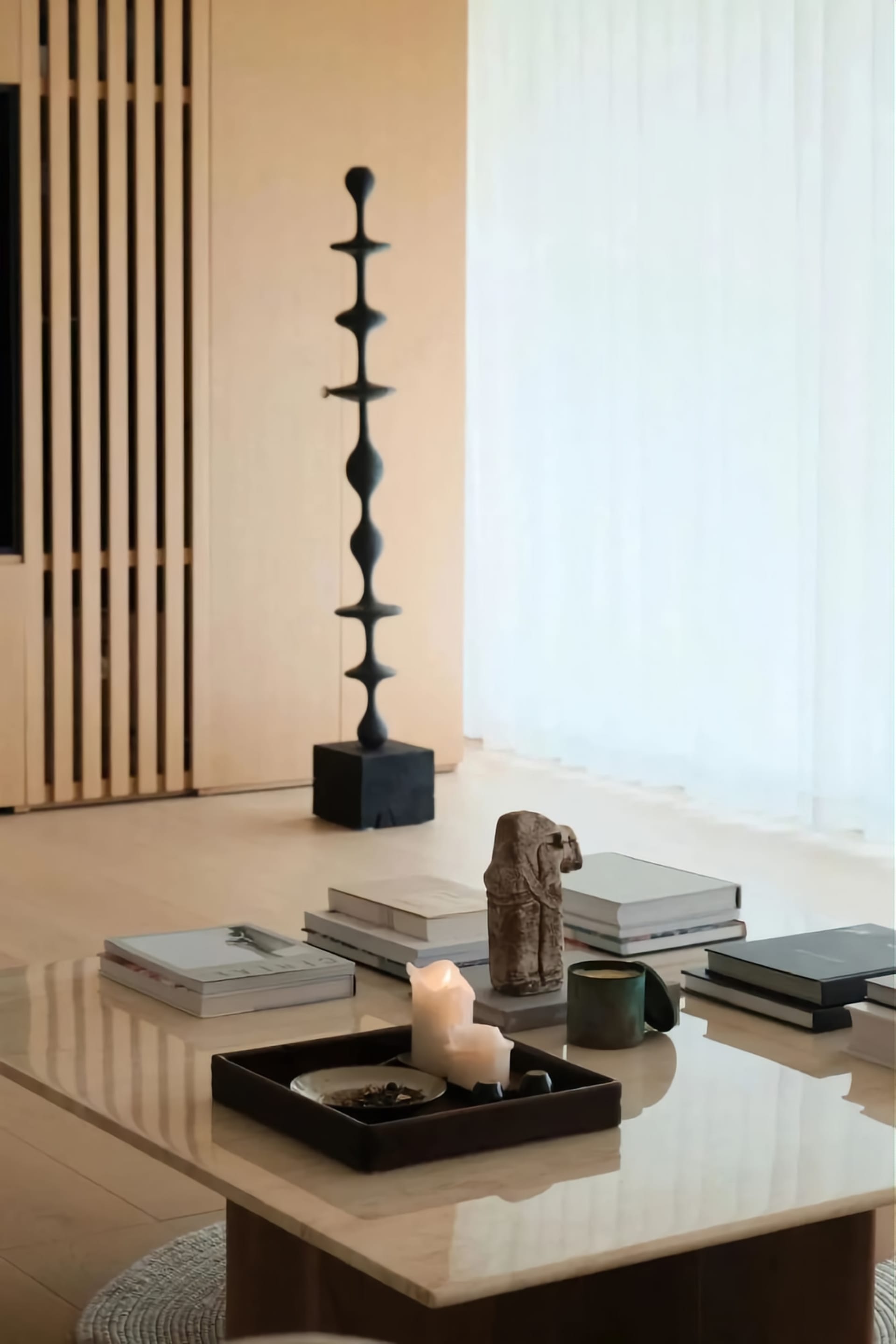 A modern coffee table with marble top, containing a candle, a bowl of snacks, and some books and a mug.
