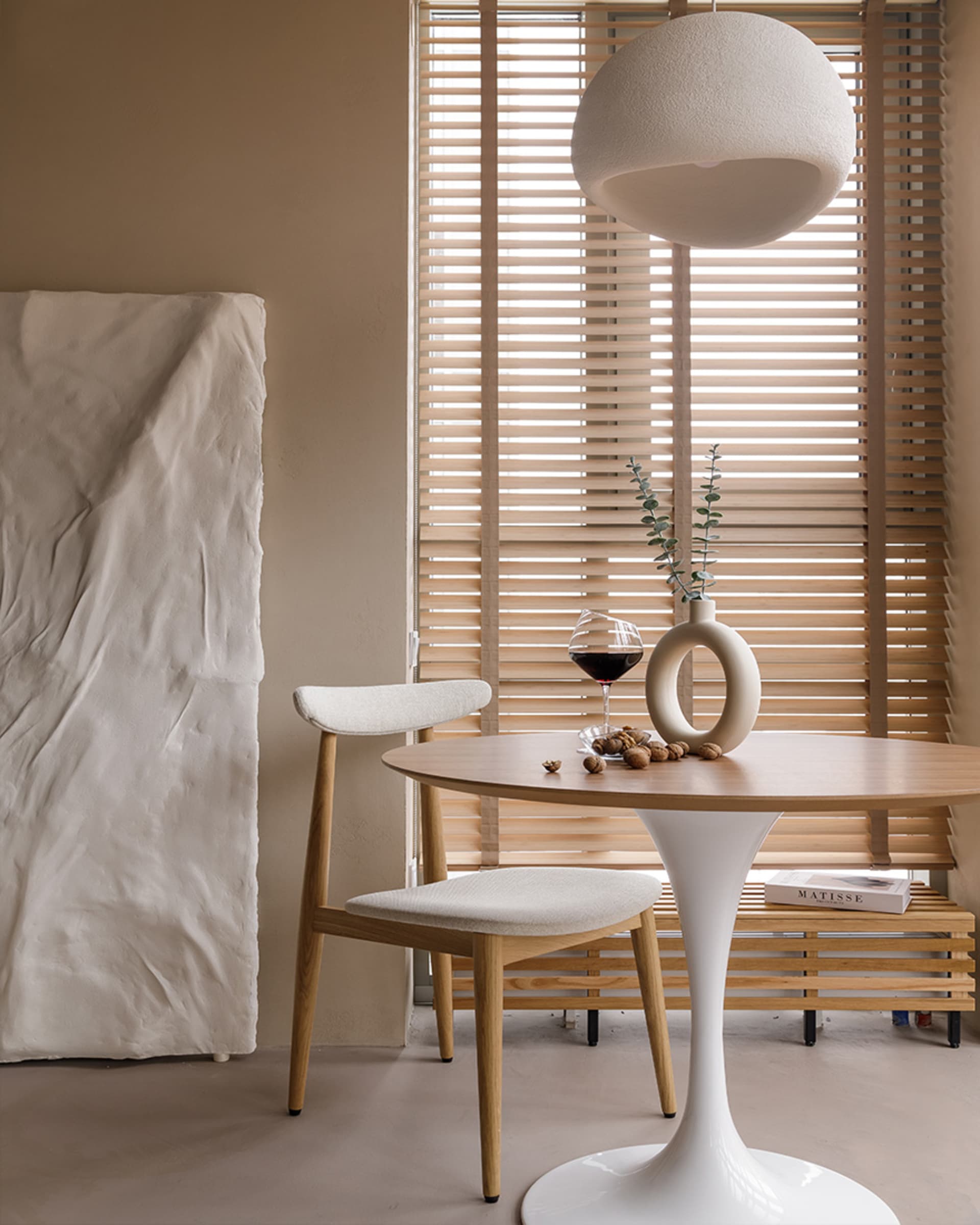 Contemporary dining area featuring a minimalist design with white fabric upholstery and wooden elements, including a round ta