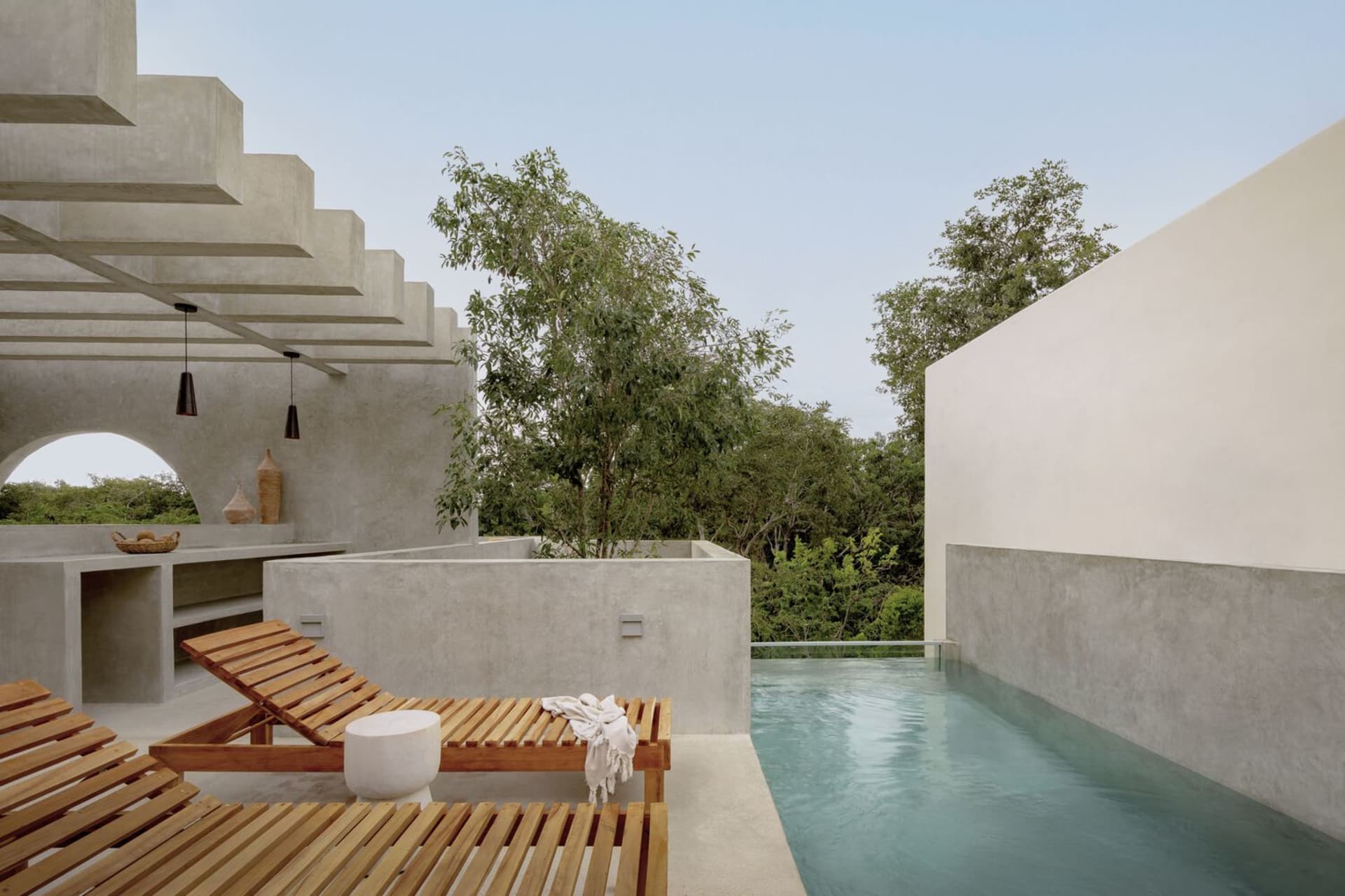 A serene modern poolside area with concrete structures and natural surroundings.