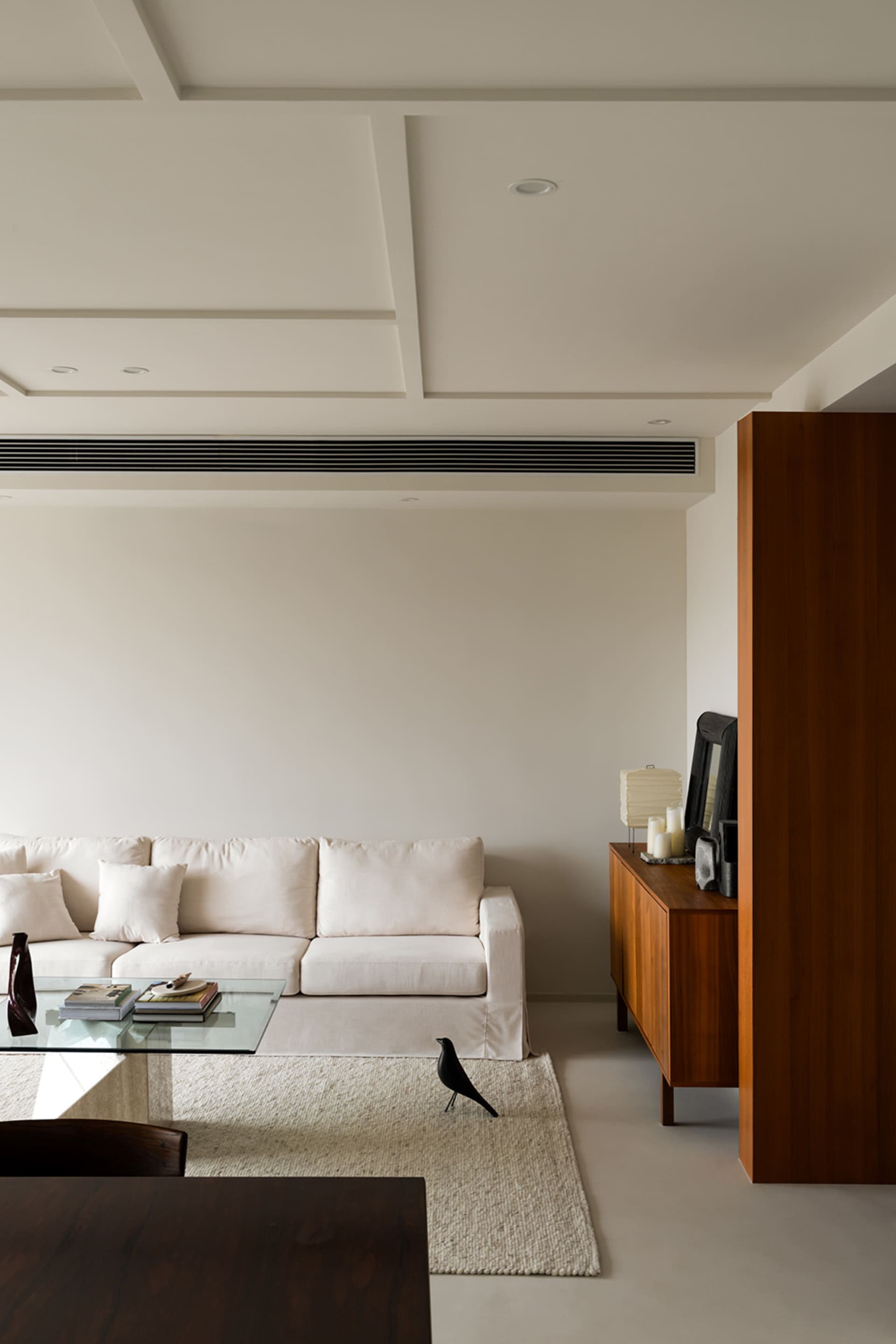 A minimalist living room featuring a white sofa, a wooden cabinet, and a glass coffee table.