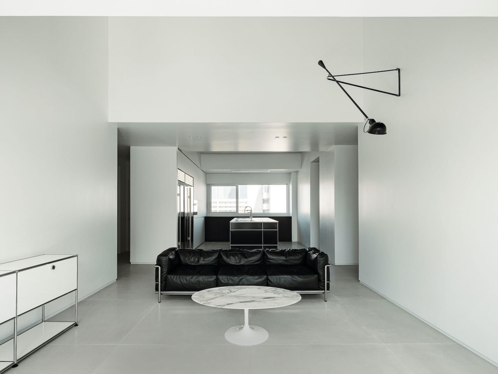 A minimalist living room with a black leather couch, white marble coffee table, and sleek, metallic furnishings.